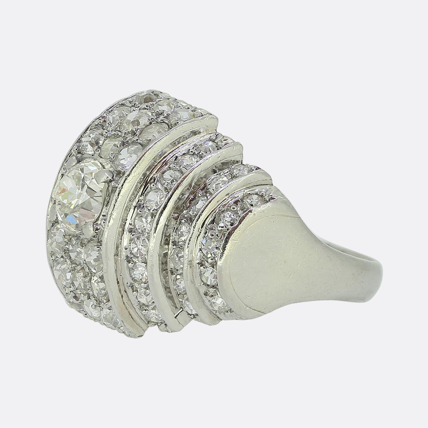 Hier haben wir einen fabelhaften Diamant-Cluster-Ring aus den 1940er Jahren. In der Mitte der gewölbten Vorderseite dieses Rings befindet sich ein einzelner runder, facettierter Diamant im Altminenschliff von 0,46 Karat. Dieser Hauptstein ist von