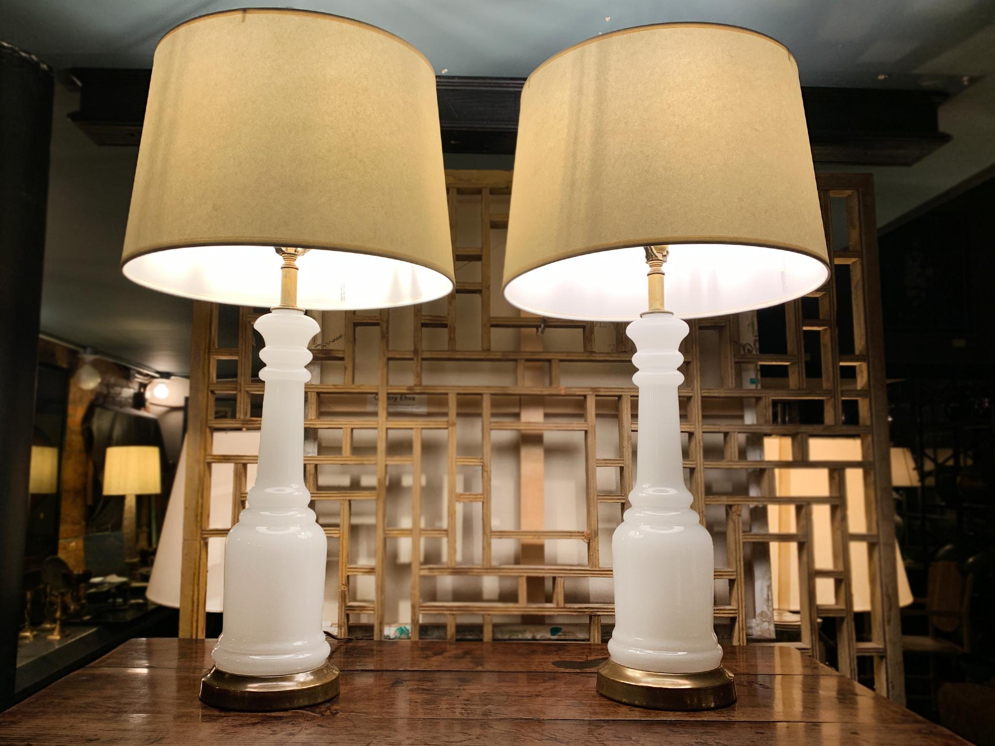 An elegant pair of opalescent glass table lamps. This pair was crafted in the 1940s. They have a simple column form that culminates in a circular brass base and are topped with acorn-shaped finials. We love how the opalescent glass has a milky