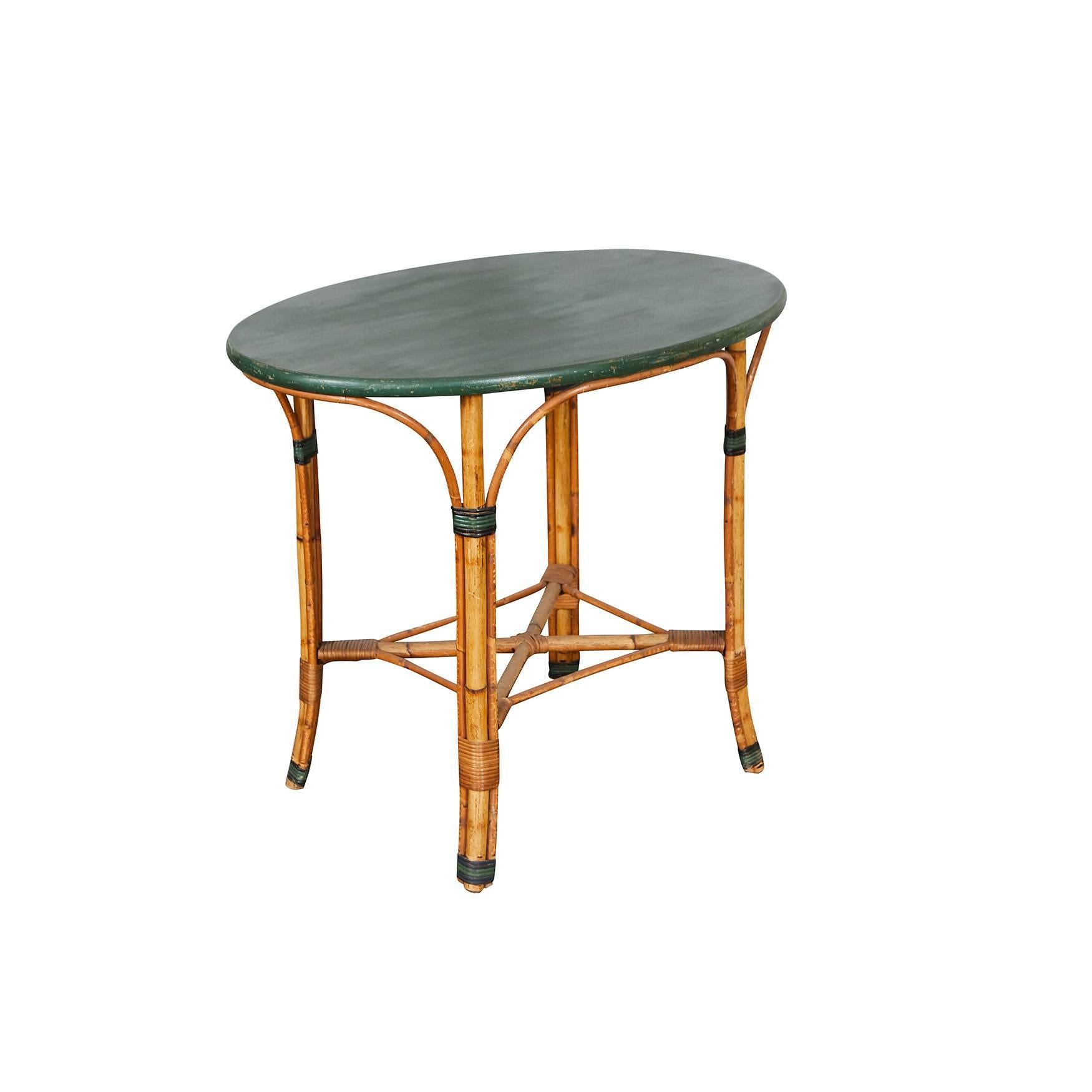 This 1940s table has a green painted solid wood oval top and bamboo legs. The table has the original painted finish with natural signs of age and wear. Note the nice black and green painted pattern on the reed bands on each leg. 



