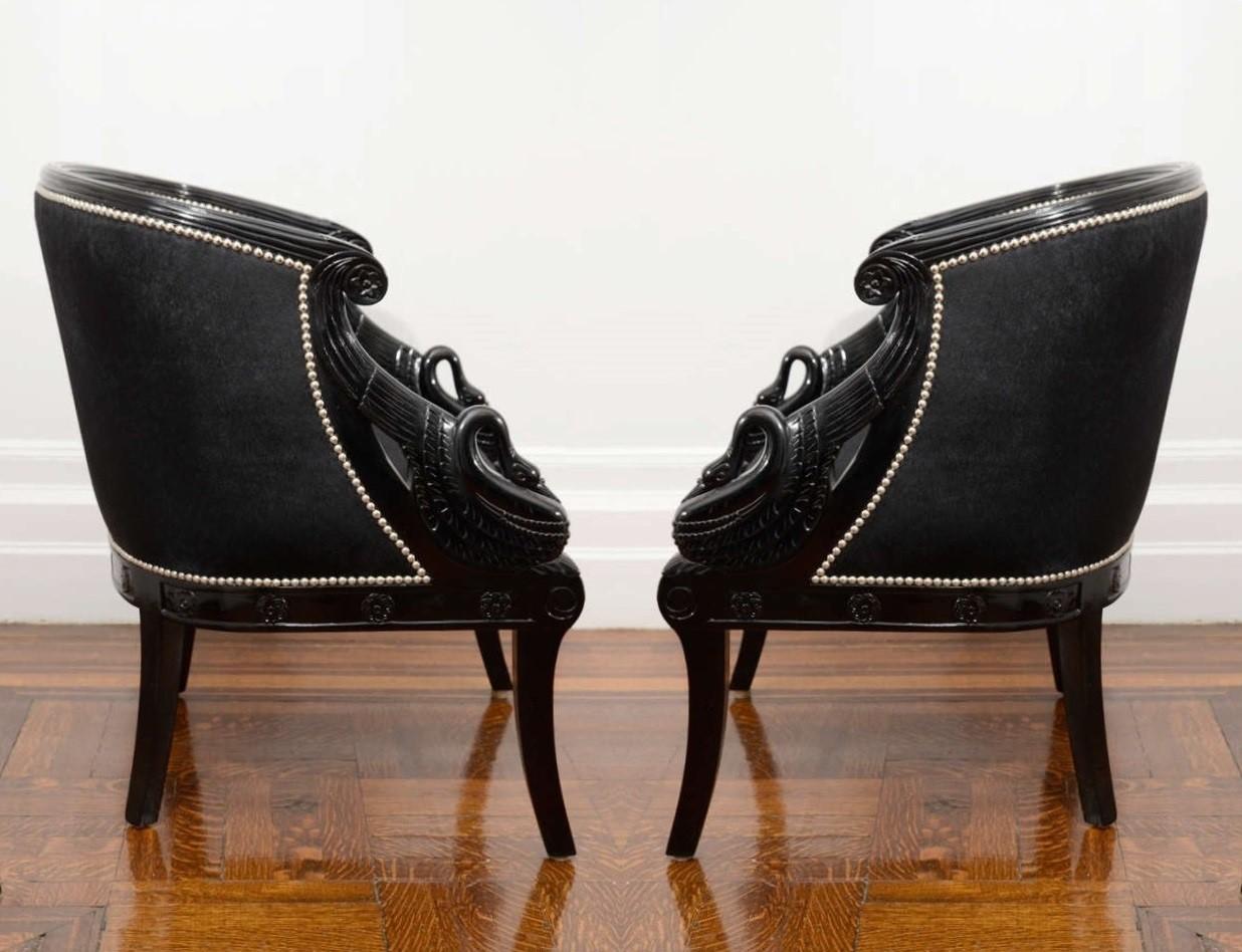 Paar neoklassische Sessel in schwarzer Lackierung, um 1940. Jedes hat eine runde geriffelte Kammschiene, die sich zu geschnitzten Rosettenarmenden fortsetzt. Aufrecht stehende geschnitzte Schwäne verbinden die neu gepolsterten Rücken- und Sitzkissen