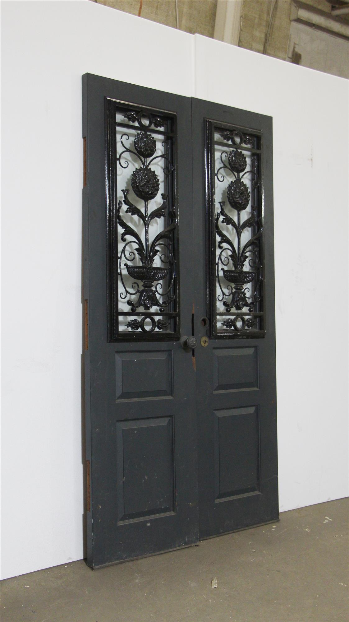 Blue painted wood doors from the 1940s with one vertical glass lite and newer decorative wrought iron window guards on the front. There are two wood panels on the bottom. The doors are painted brown on the opposite side. Some slight cracks in wood.