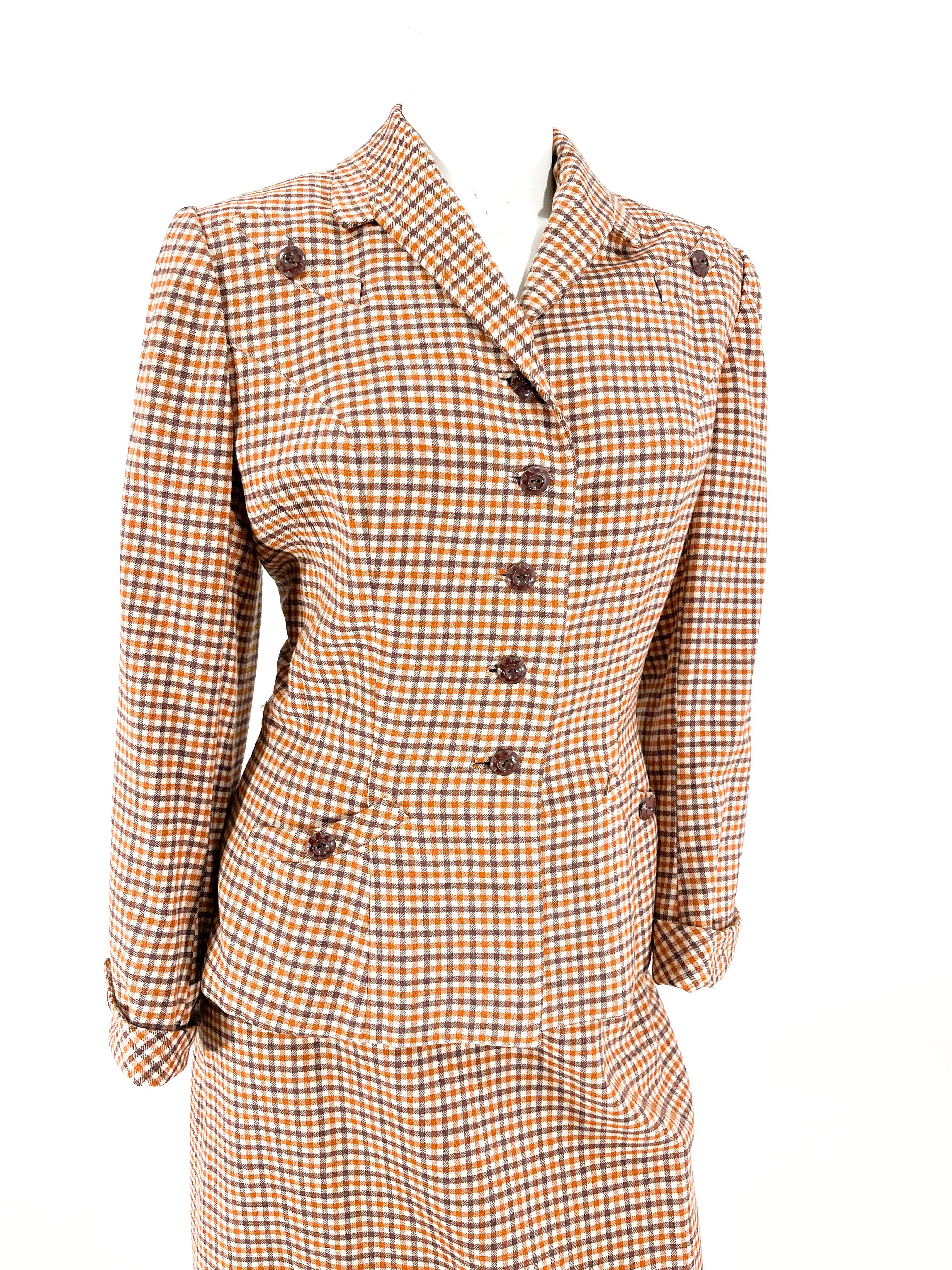 Weiß, braun und rostfarben karierter Wollanzug mit Rock aus den 1940er Jahren. Die Jacke des Anzugs hat einen modifizierten Kragen mit Kerbe, gepolsterte Schultern, zwei obere Faux-Smile-Taschen, schokoladenbraune Knöpfe, eingelassene Knopflöcher,