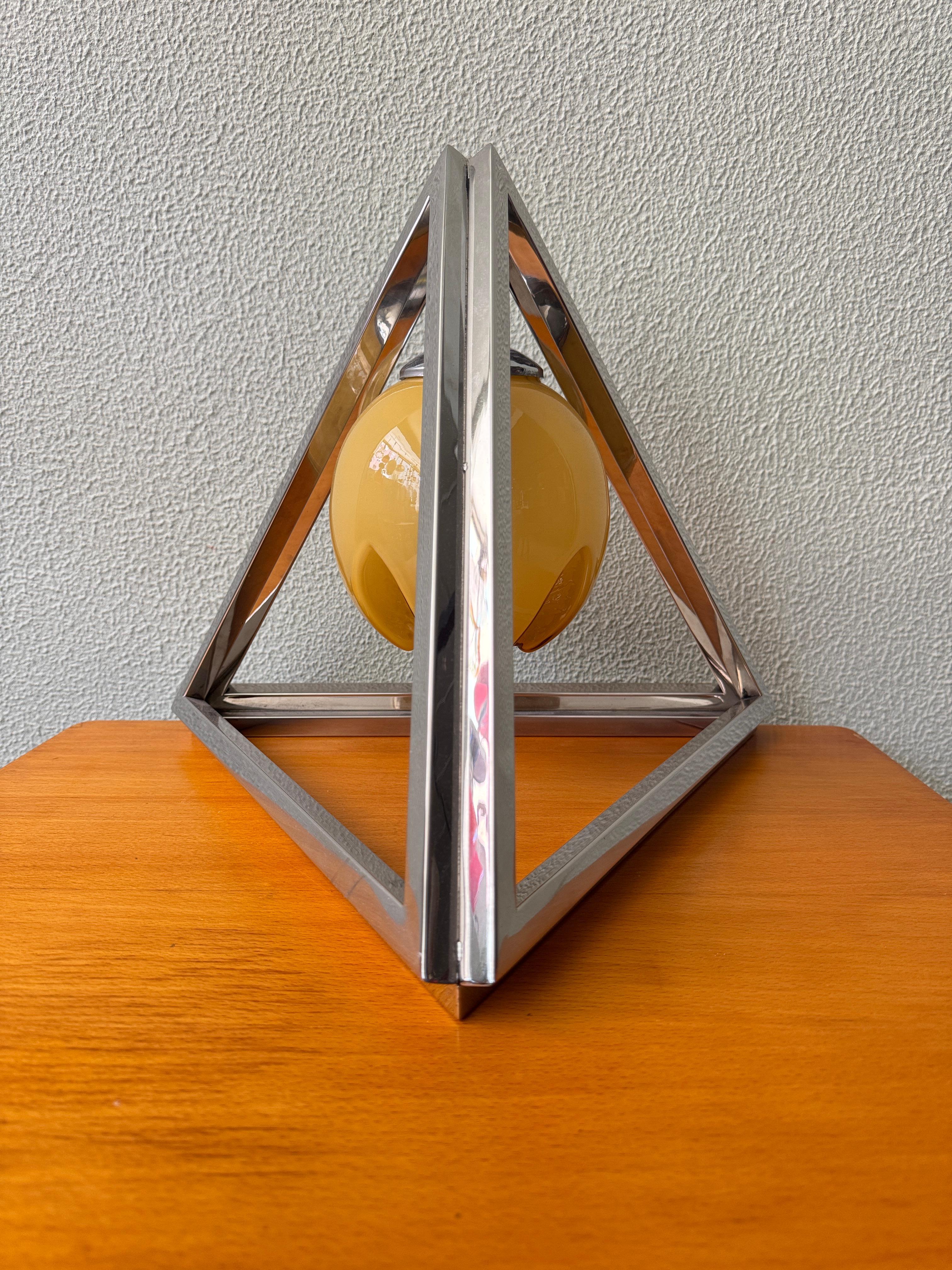 Esta rara lámpara de mesa portuguesa de la década de 1940 es un sorprendente ejemplo de diseño Art Déco, que combina el rigor geométrico con la elegancia escultórica. Su estructura piramidal triangular, elaborada en latón cromado, forma un audaz
