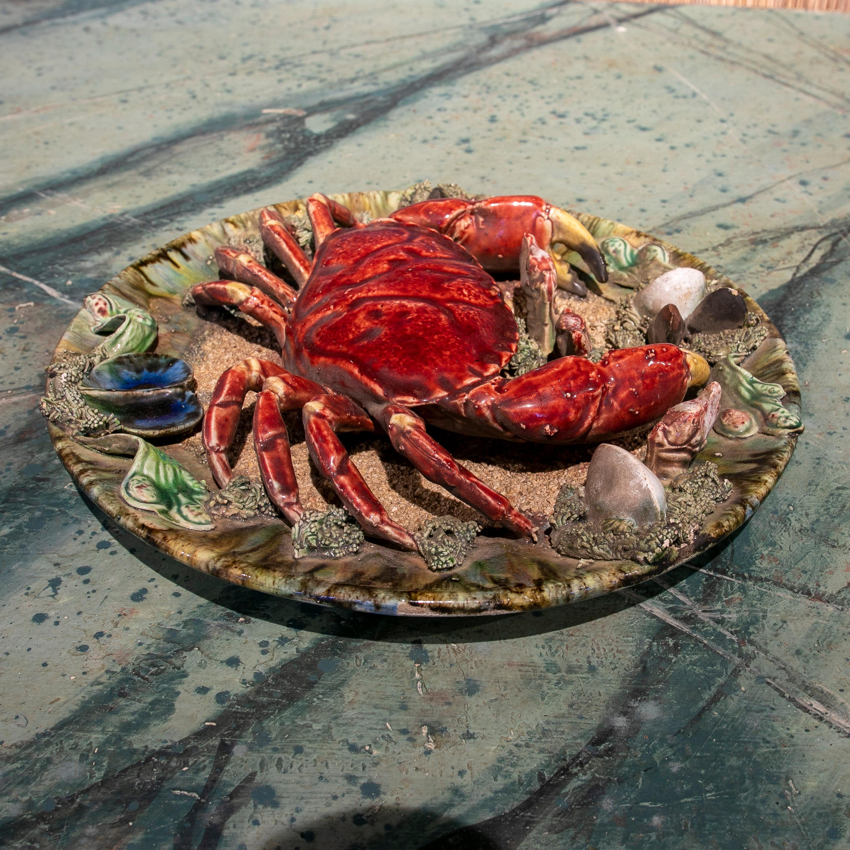 Portuguese Majolica Palissy ware wall plate 32 cm, signed Caldas da Rainha, circa 1940, featuring a large crab foremost and centre, on a green plate with sand, seaweed, mussels and sea shells. Colourfully glazed three dimensional ceramic plates