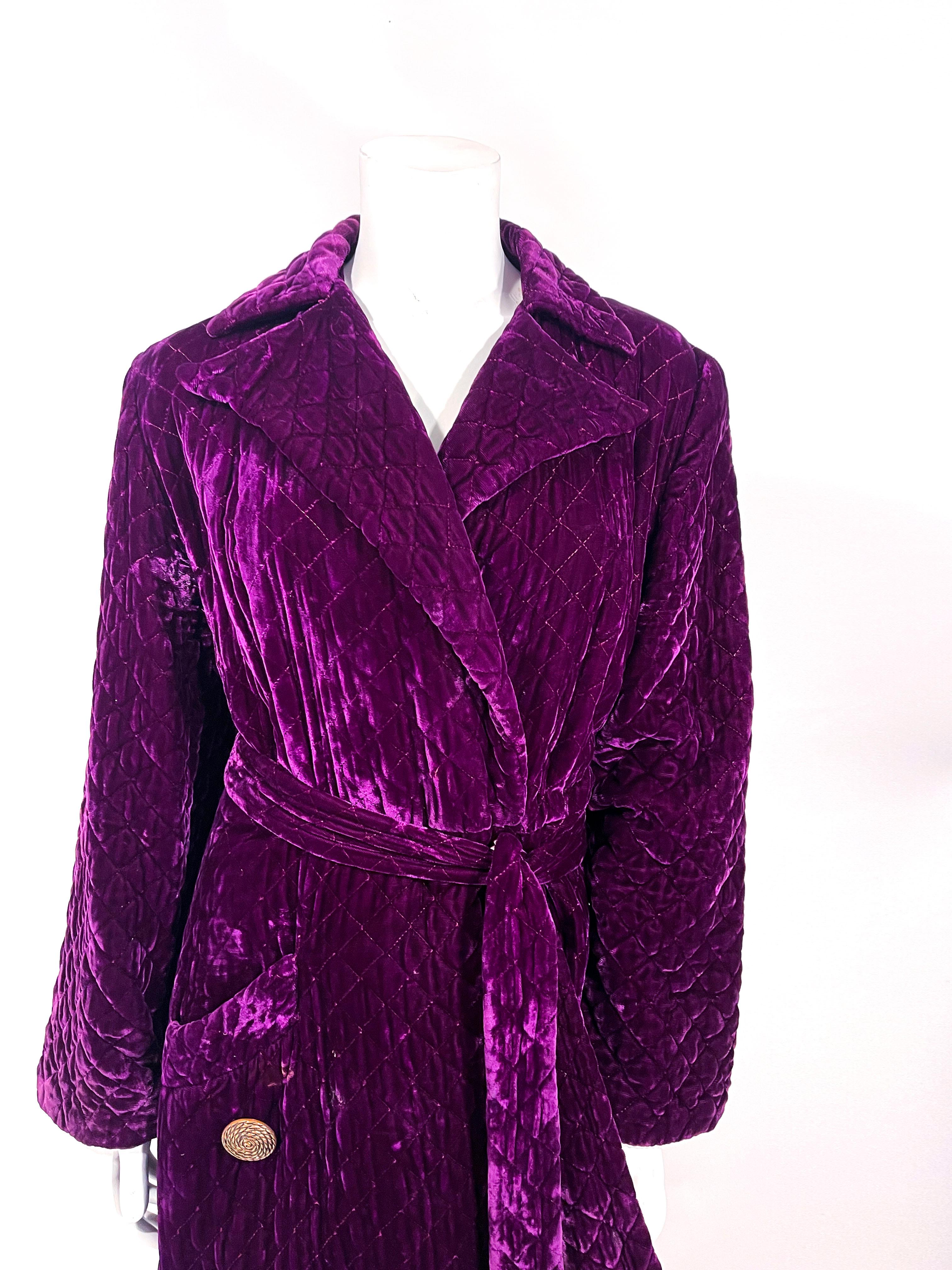 Late 1940s to early 1950s purple crushed velvet quilted house robe with original belt, a single deep patch pocket decorated with a large copper button, padded full-length sleeves, and peak lapel collar. The interior is fully lined with with an inner
