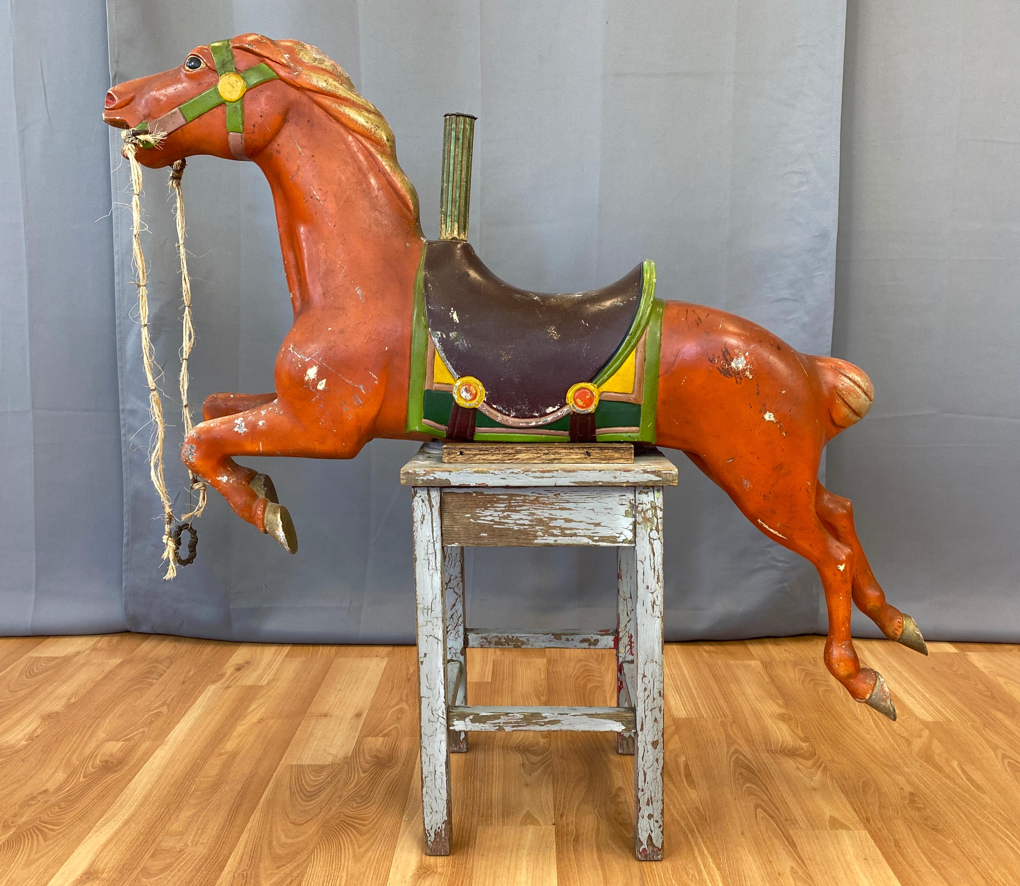 A wonderful whimsical circa 1940s painted metal carousel horse. 
Nicely made with it's main body colored in a burnt red, and a brown, green and yellow saddle.
Poise of the horse, is like it's jumping over a fence, has a newer custom halter, and