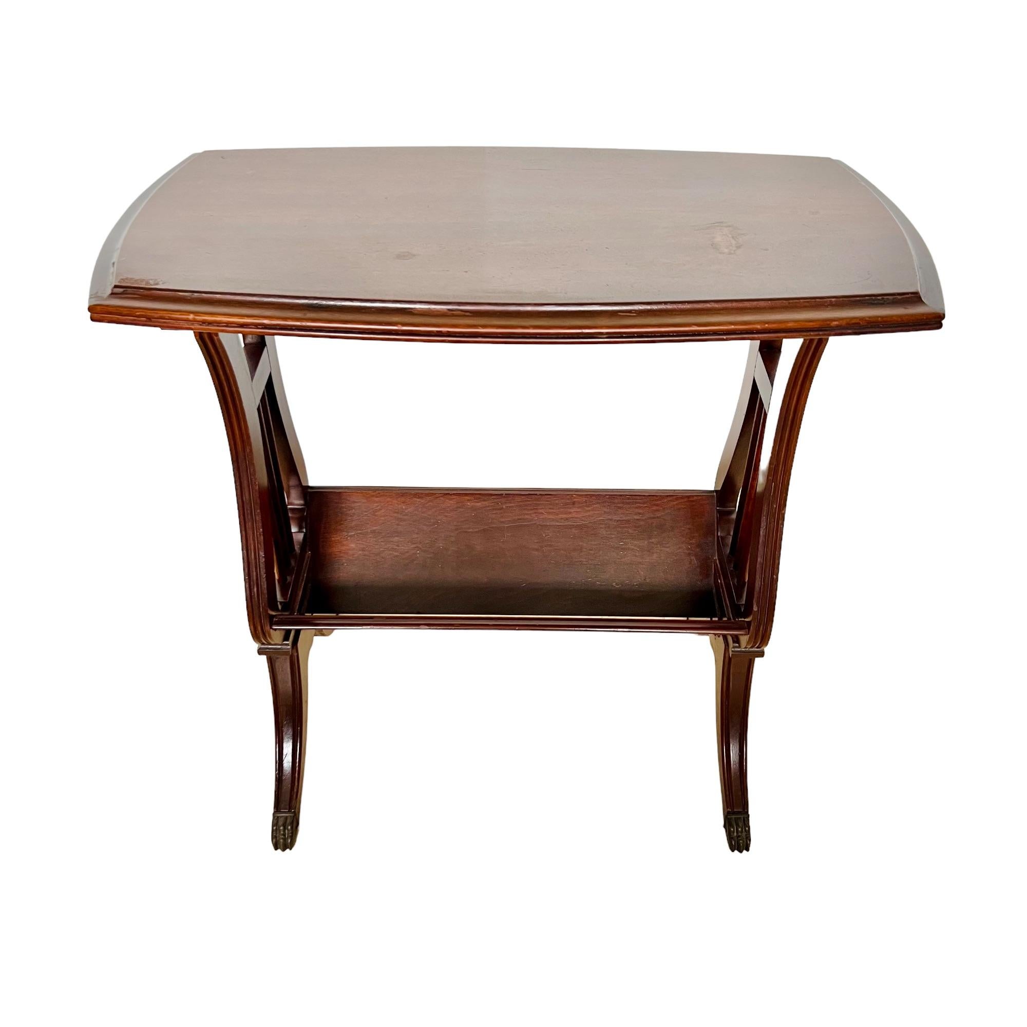 A vintage English Regency style mahogany lyre accent table. Featuring a rectangular top surface with ogee edge, a lower bookshelf supported by harp form ends and channeled saber legs with brass capped paw feet.

Dimensions: 24