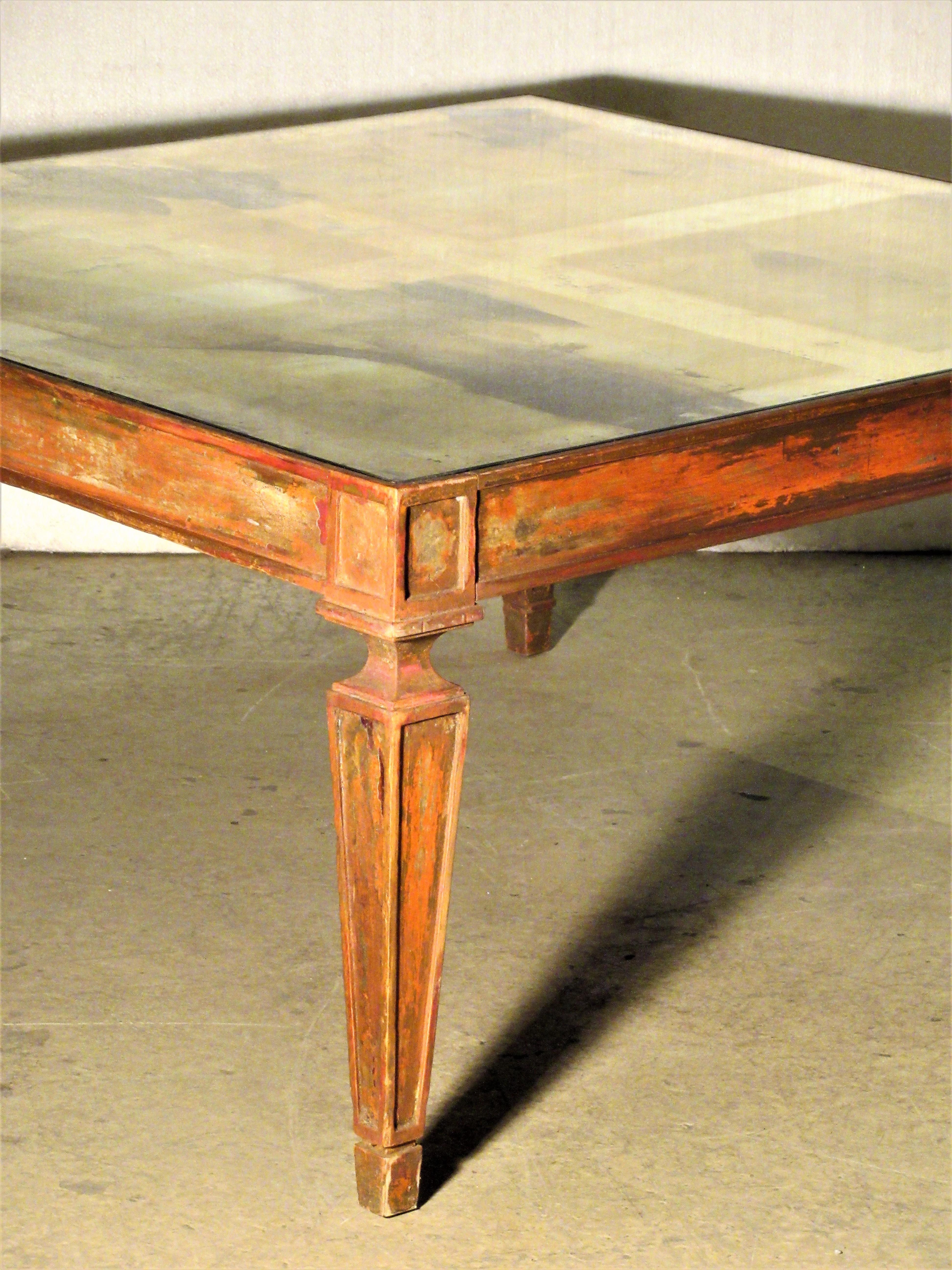 1940s Classical Regency style big square coffee table with the original highly oxidized grid pattern design mirrored top. The wood base has been stripped and scraped down to the old red bold painted surface revealing a wide range of colors and very