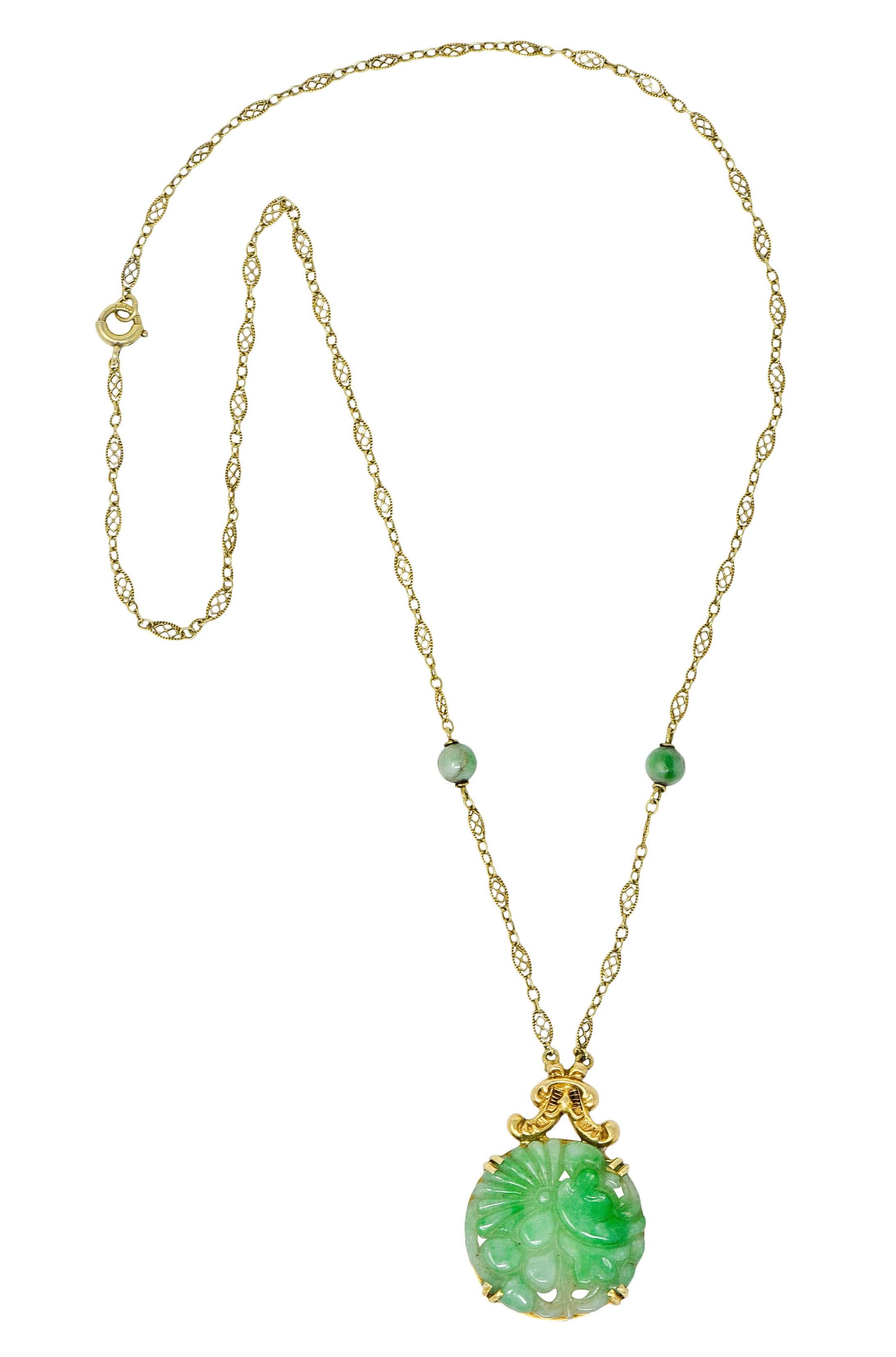 Circular pendant is comprised of deeply carved jade, depicting a floral and foliate motif

Translucent and mottled very light green to green in color

With a gold foliate surmount suspended from a delicately pierced link chain necklace

Accented by