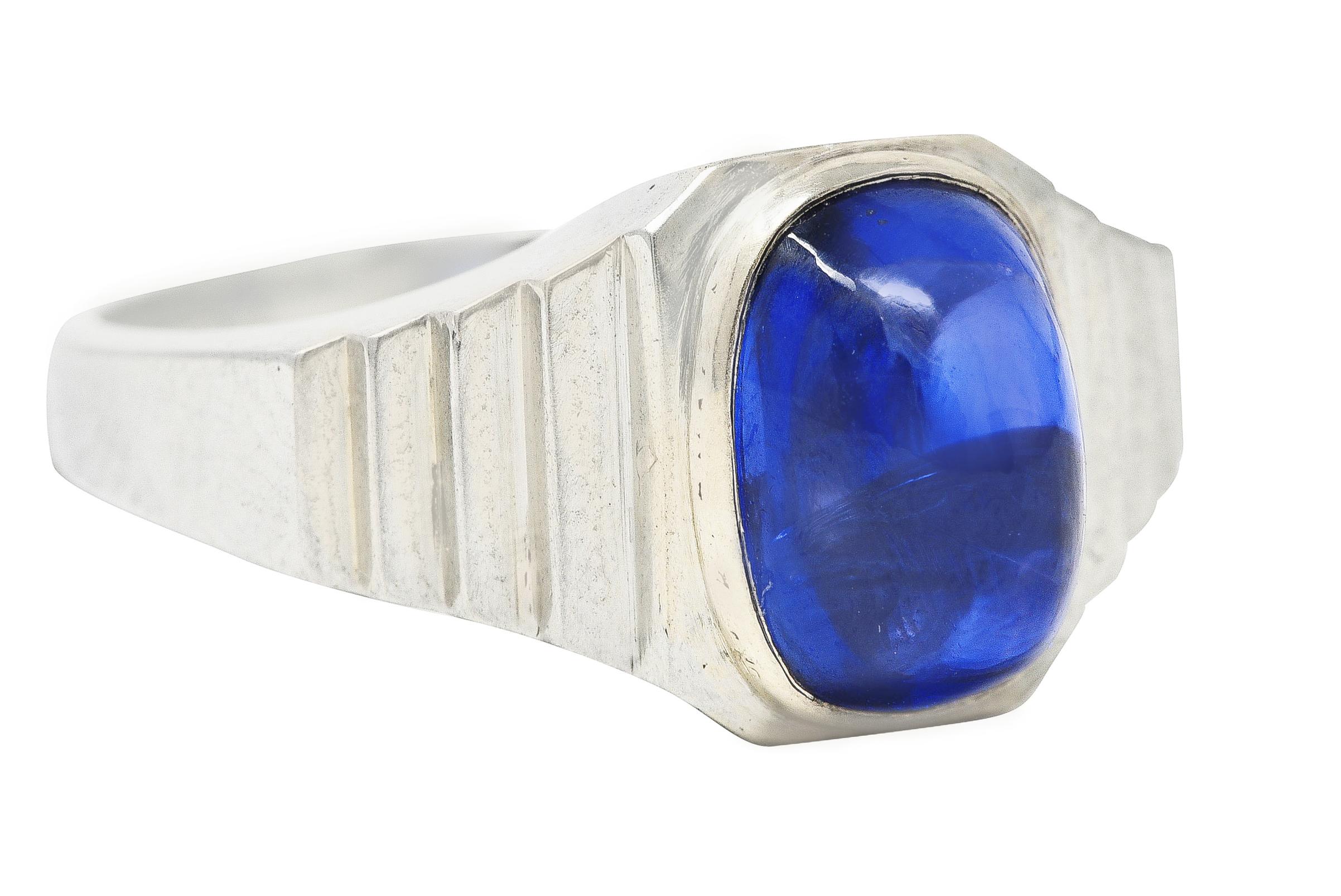 Band ring centers a highly domed sapphire cushion cabochon weighing approximately 5.15 carats. Transparent and violetish blue in color - medium saturation. Bezel set in a polished white gold surround and flanked by faceted stepped shoulders. Stamped