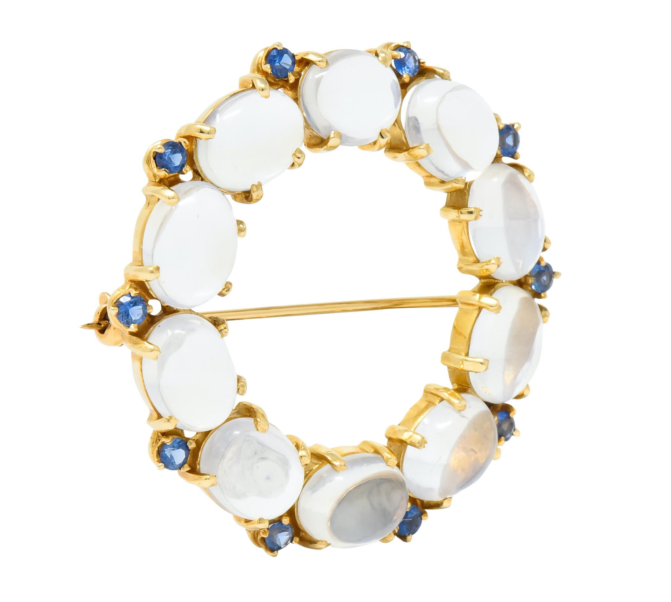 Wreath style brooch comprised of ten oval cabochon moonstones measuring approximately 9.0 x 6.5 mm, transparent with strong billowing blue adularescence 

Accented by round cut sapphire weighing approximately 1.00 carat total, transparent and