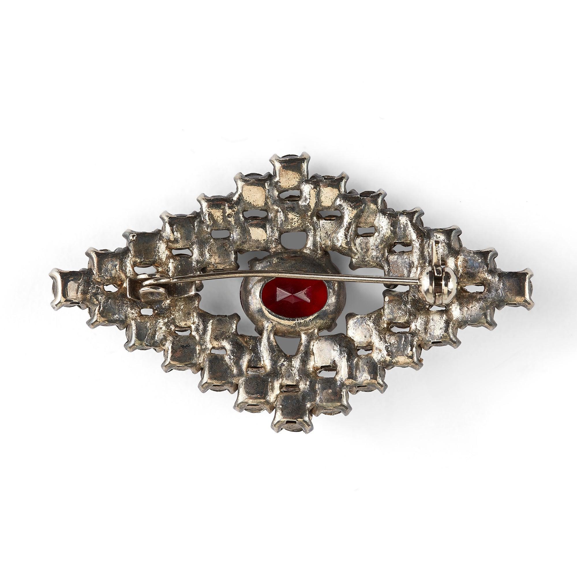 Diese originelle Kostümbrosche aus den 1940er Jahren zeichnet sich durch eine sehr große Anzahl klarer Strasssteine im Brillantschliff aus, die alle einzeln mit Zacken besetzt sind. Der große zentrale Stein ist einem Rubin nachempfunden und in