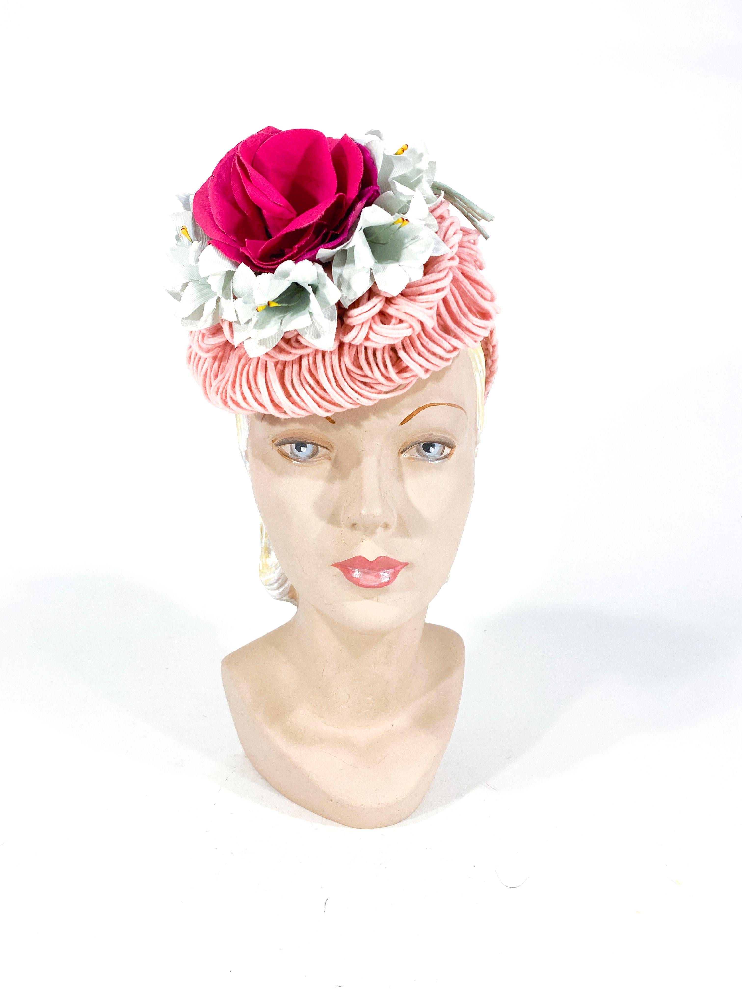 1940's handmade rose pink crochet wool cocktail hat with layers of wool loops, pale blue flowers, and centered with a large dark silk rose with velvet petals. The security ring fixes the hat on to the head and is covered with decorative crochet. 