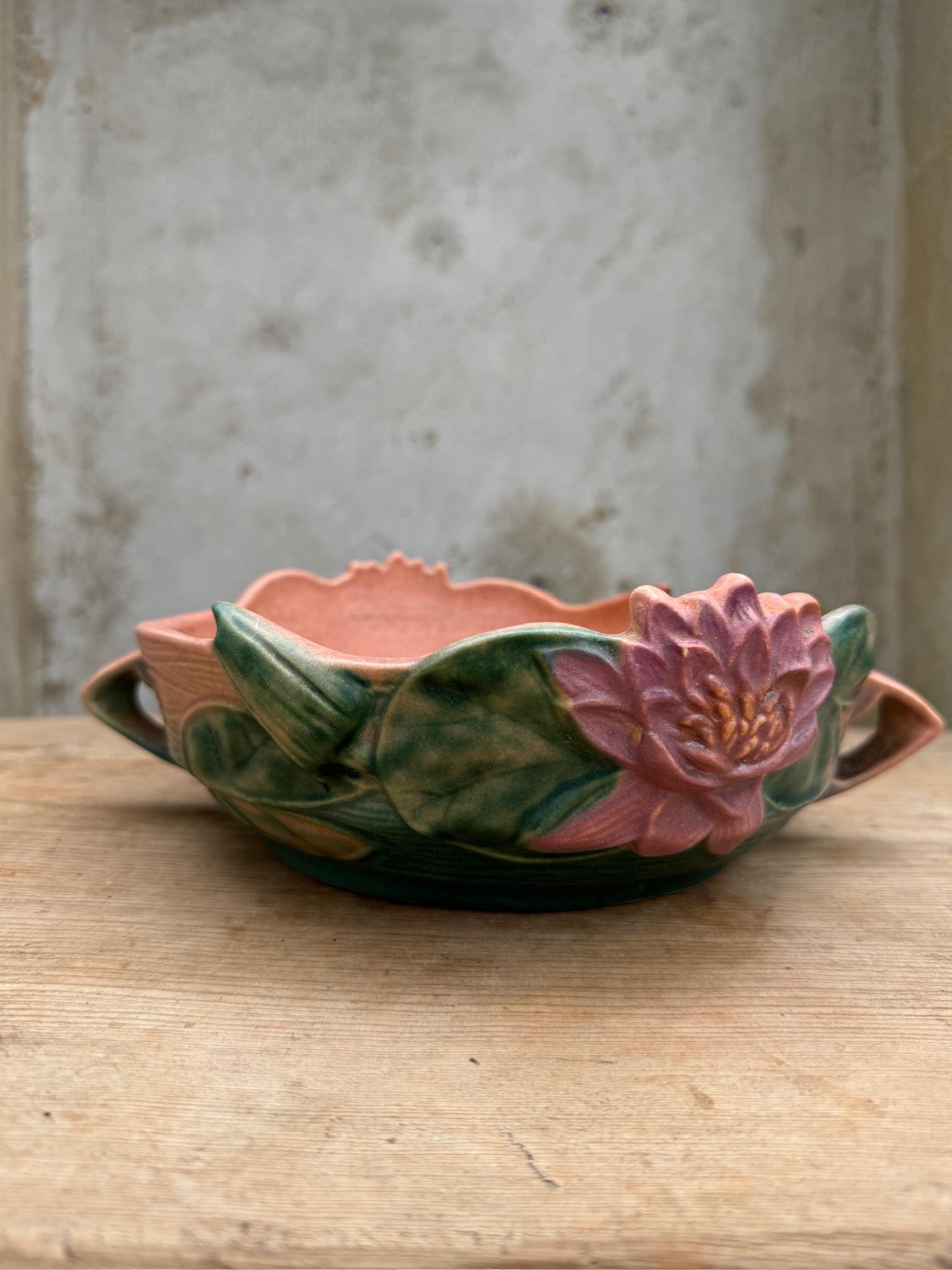 Le bol de Roseville Pottery, datant des années 1940, est une charmante pièce de poterie d'art américaine. Ce bol se distingue par sa glaçure de couleur abricot et est doté de deux poignées pour une manipulation aisée. Le bol est orné d'un design