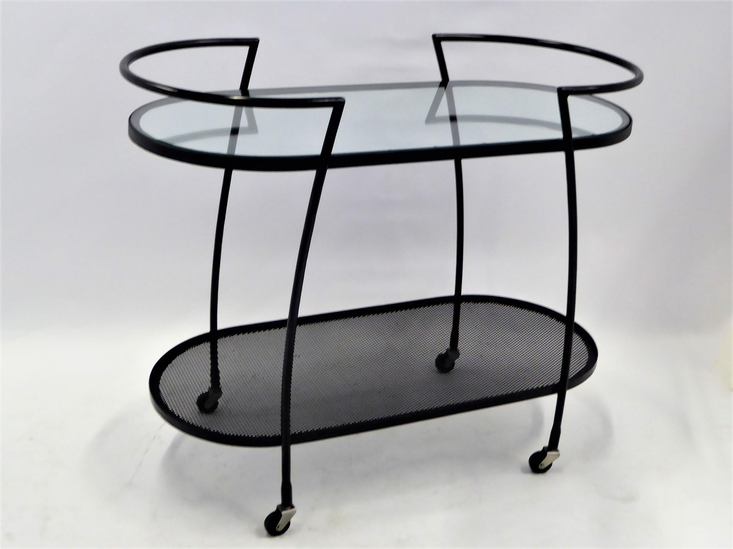 1940s streamline moderne wrought iron rolling cart with an inset glass shelf above and metal screen shelf below. The racetrack oval shape has shaped arms that continue down the sides as legs. New glass and wrought iron re-patinated. After the styles