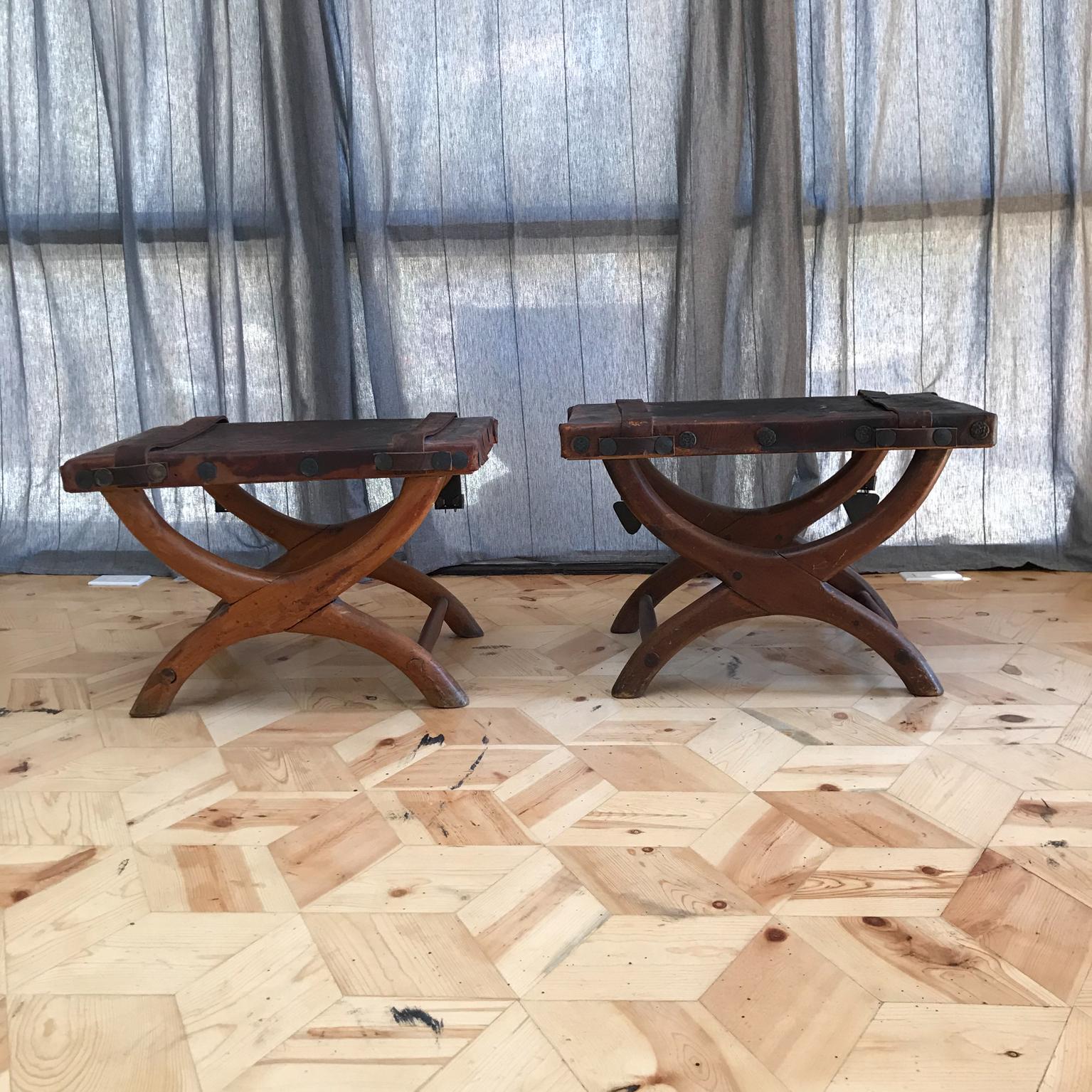 AMBIANIC presents: Vintage Spanish colonial curule stools ottoman bench, set of 2, circa 1940s. Made in Mexico.

Latin American style and manner of Clara Porset and Luis Barragan. Rustic leather seat with straps.

Features worn patina leather