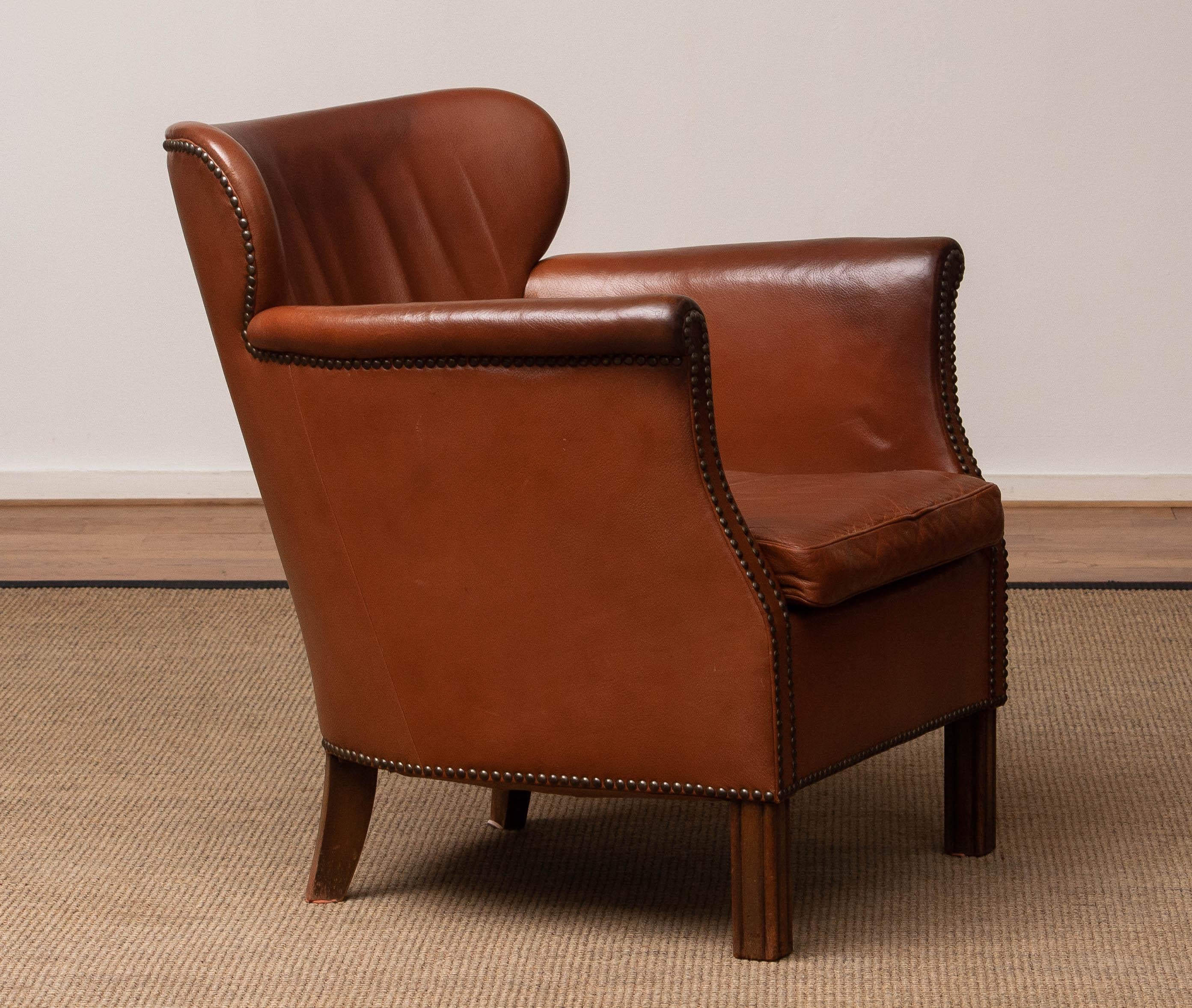 Scandinavian lounge chair from the first half of the 20th century in tan / brown nailed leather made in Denmark in allover good condition. Please note that there is made a repair inside the backrest in the past. (visible on the photo) what doen't