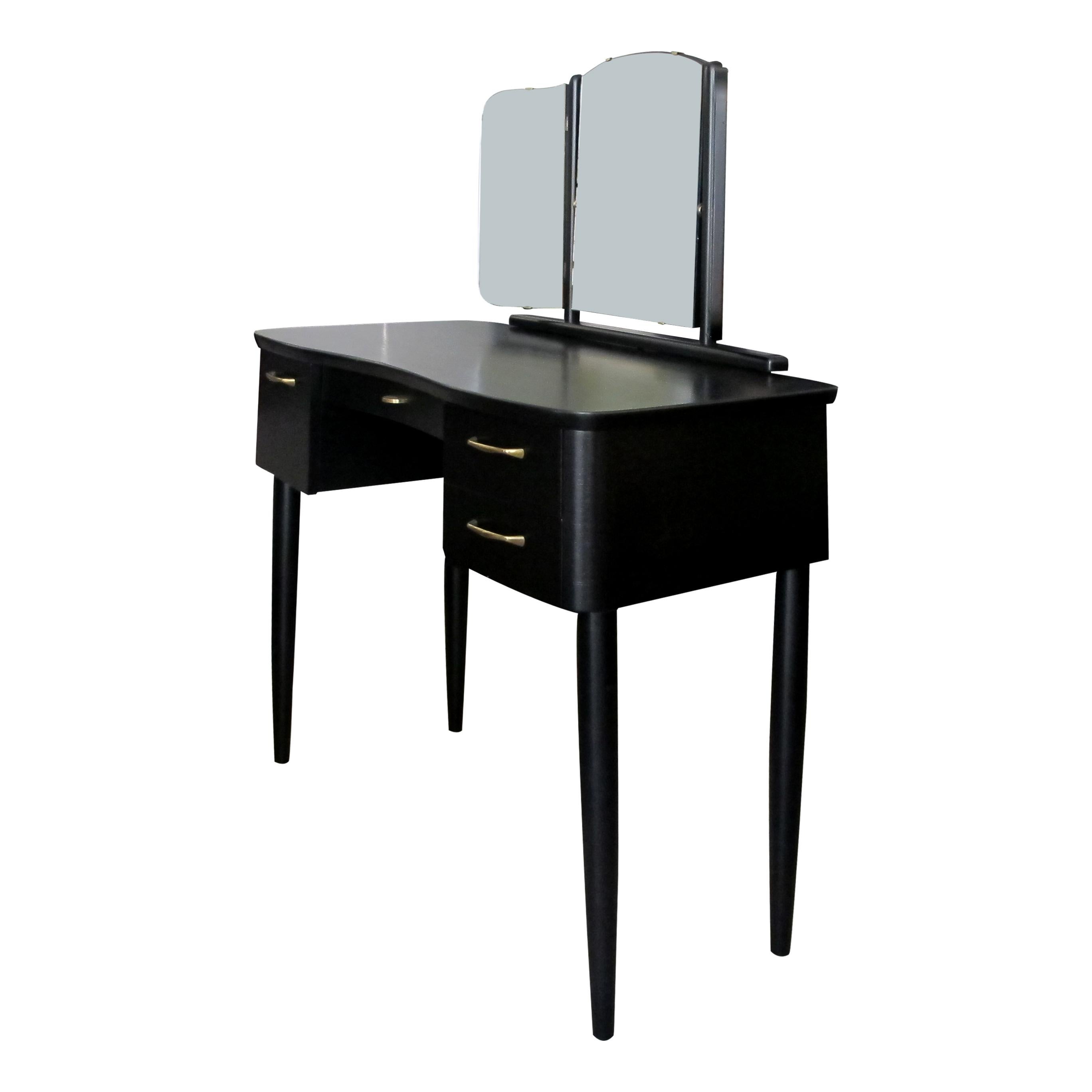 A 1940s Ebonised Scandinavian dressing table with its original triptych mirror and original feature brass handles. The dressing table has a pair of identical drawers on the right hand side, a deep single drawer on the left and a shallow central