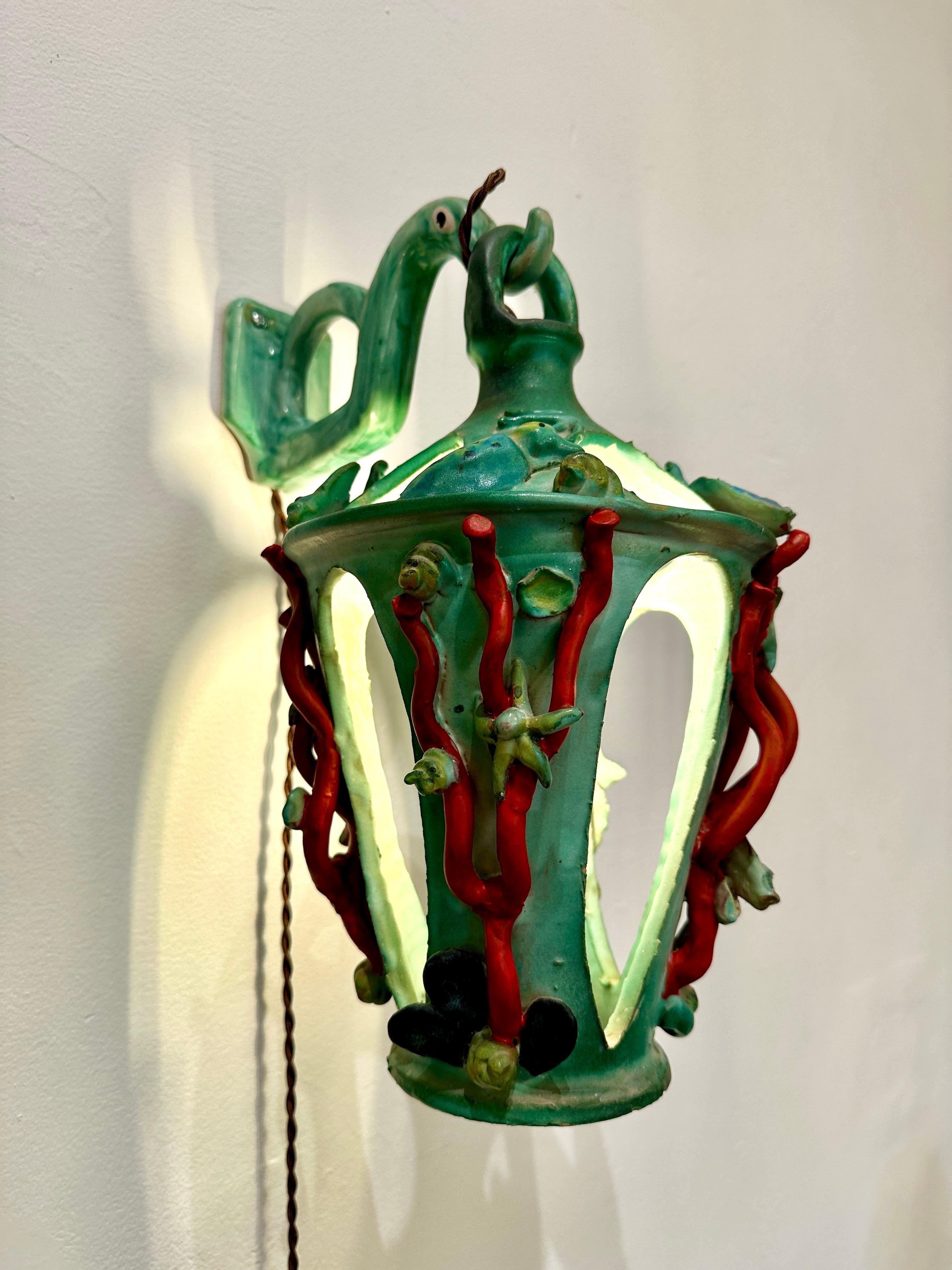 Cette lanterne murale italienne en maïolique représente des créatures marines en relief, des coraux et des algues d'un rouge éclatant.  Une seule ampoule fournit un éclairage suffisant - cette lampe peut être utilisée comme indiqué, fixée au mur OU