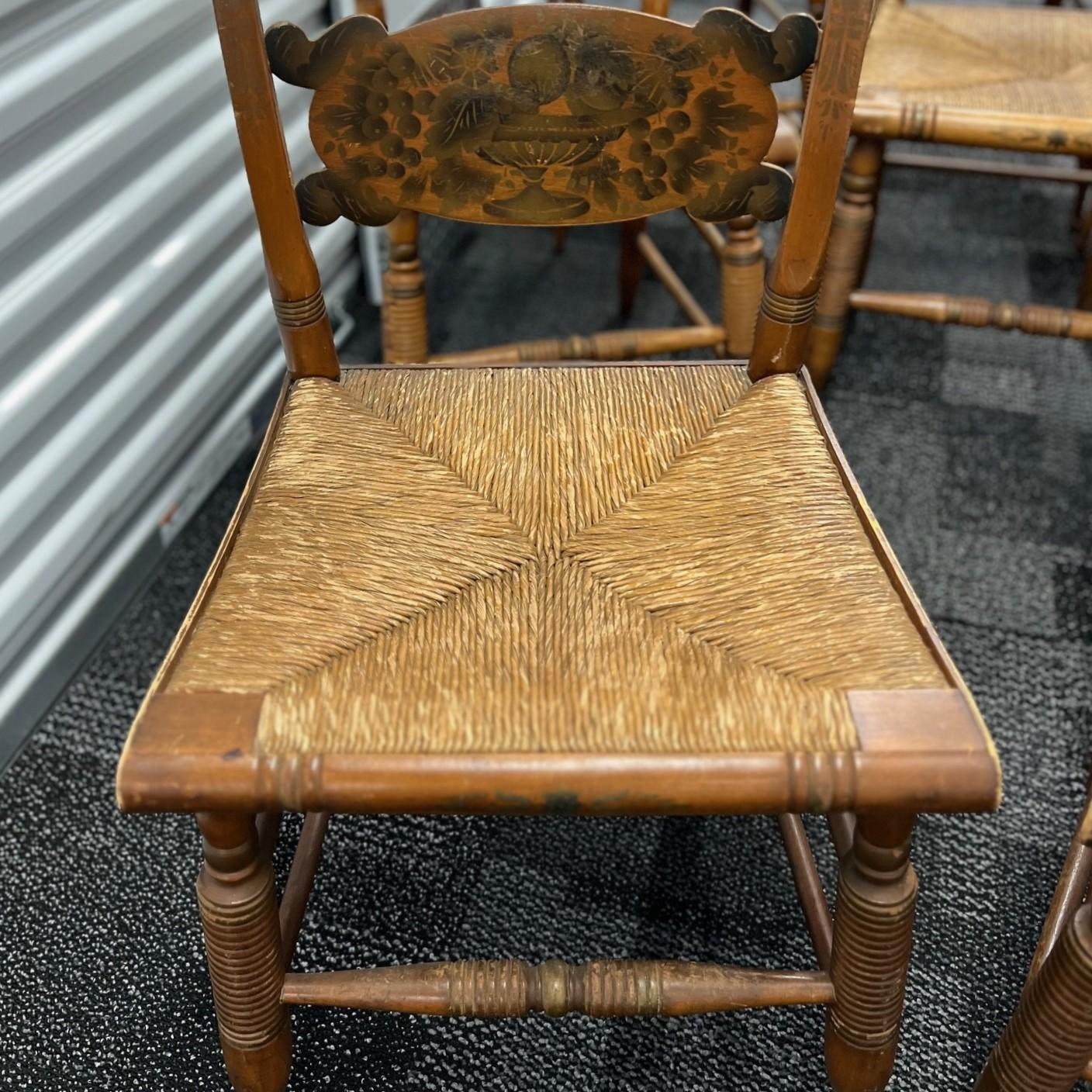 A charming set of eight vintage Hitchcock chairs, featuring handwoven rush seats and classic stenciled fruit motifs on the backrests. These chairs were produced by the Hitchcock Chair Company of Connecticut, a legendary American furniture maker