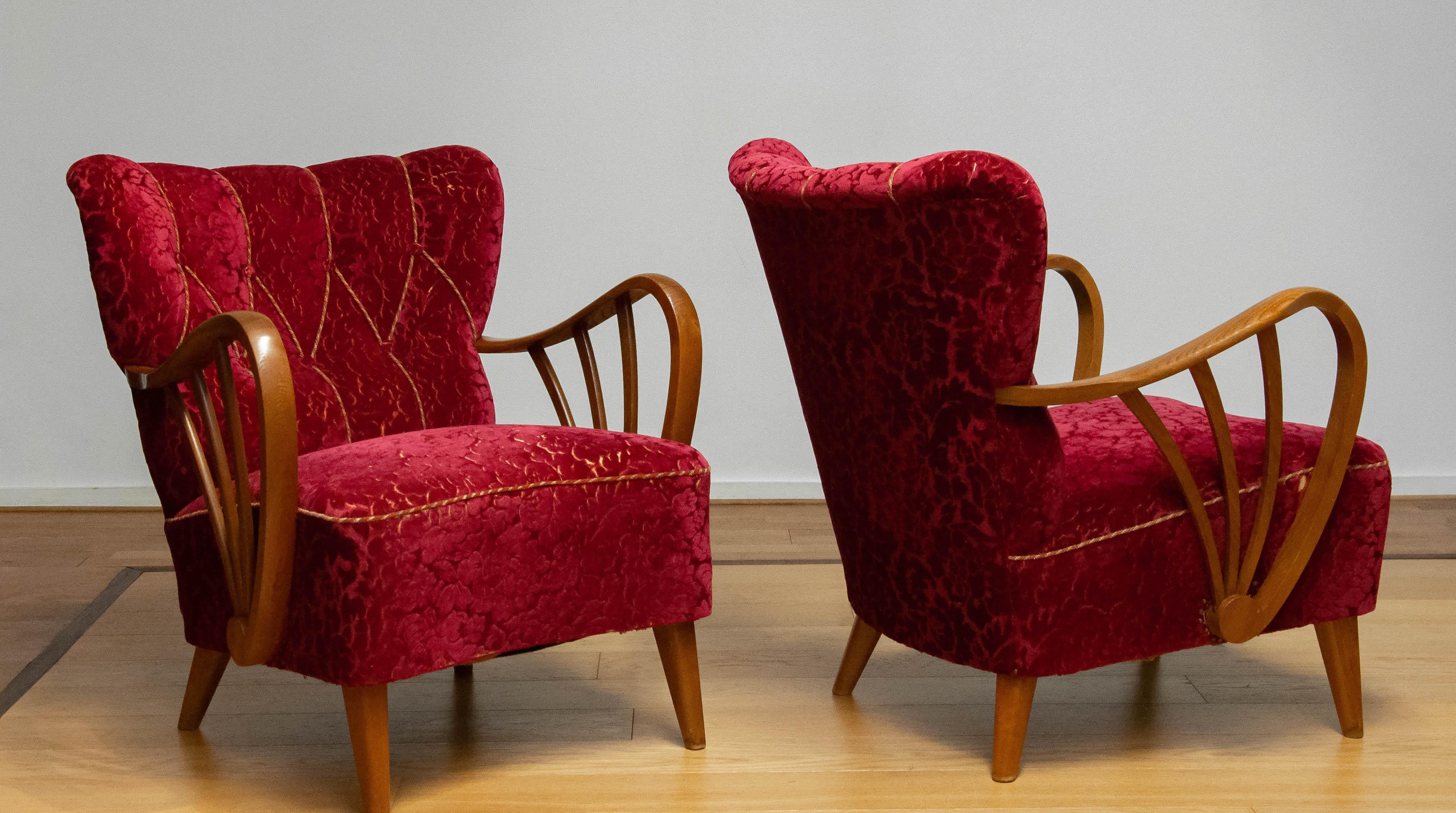 This is a set of armchairs manufactured by Sternells in Virserum, Sweden, during the 1940s.
The chairs feature their original luxurious velour upholstery in a deep red tone, beautifully complemented by sculptural armrests and a solid oak frame. The