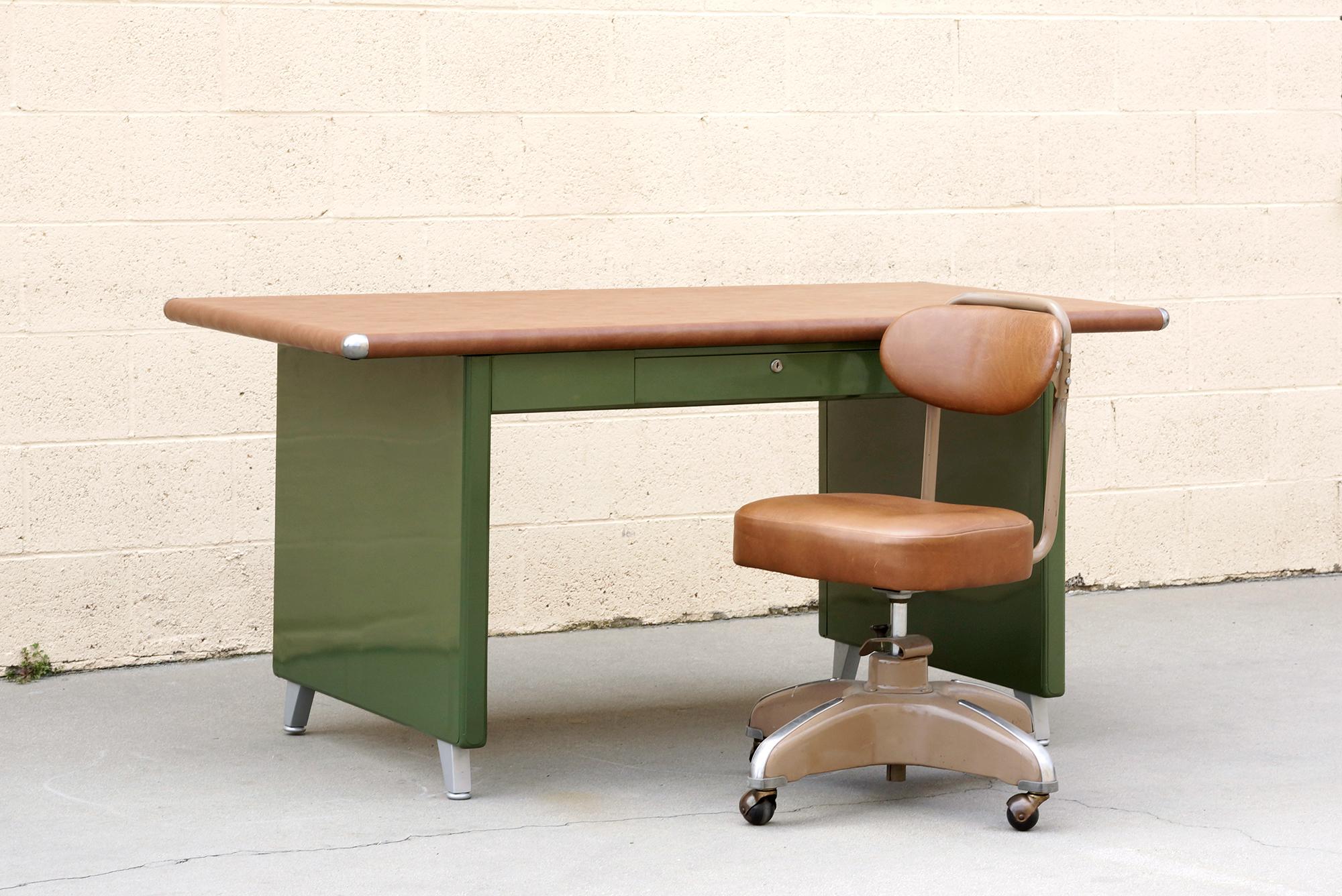 What a beauty! We refinished this rare 1940s Shaw Walker panel leg tanker table in an army green powder coat with a camel-colored vinyl top. Original splayed legs powder coated in metallic silver; polished steel table-top bumpers. Features a single