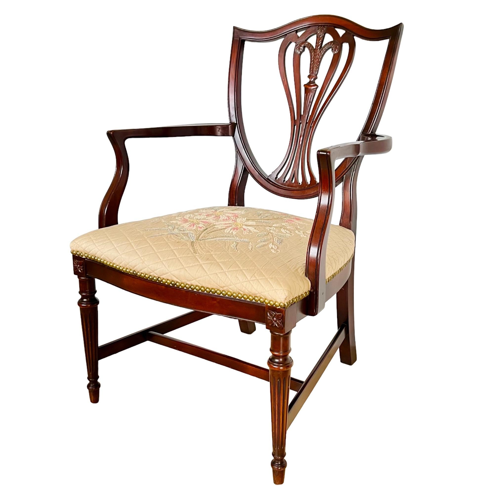 A George III style decorative mahogany armchair by Grand Ledge Chair Co. circa 1945. Sheraton design featuring a carved shield back, tapered fluted front legs and channeled arm & back detail. Hand stitched diamond quilted tan beige fabric seat with