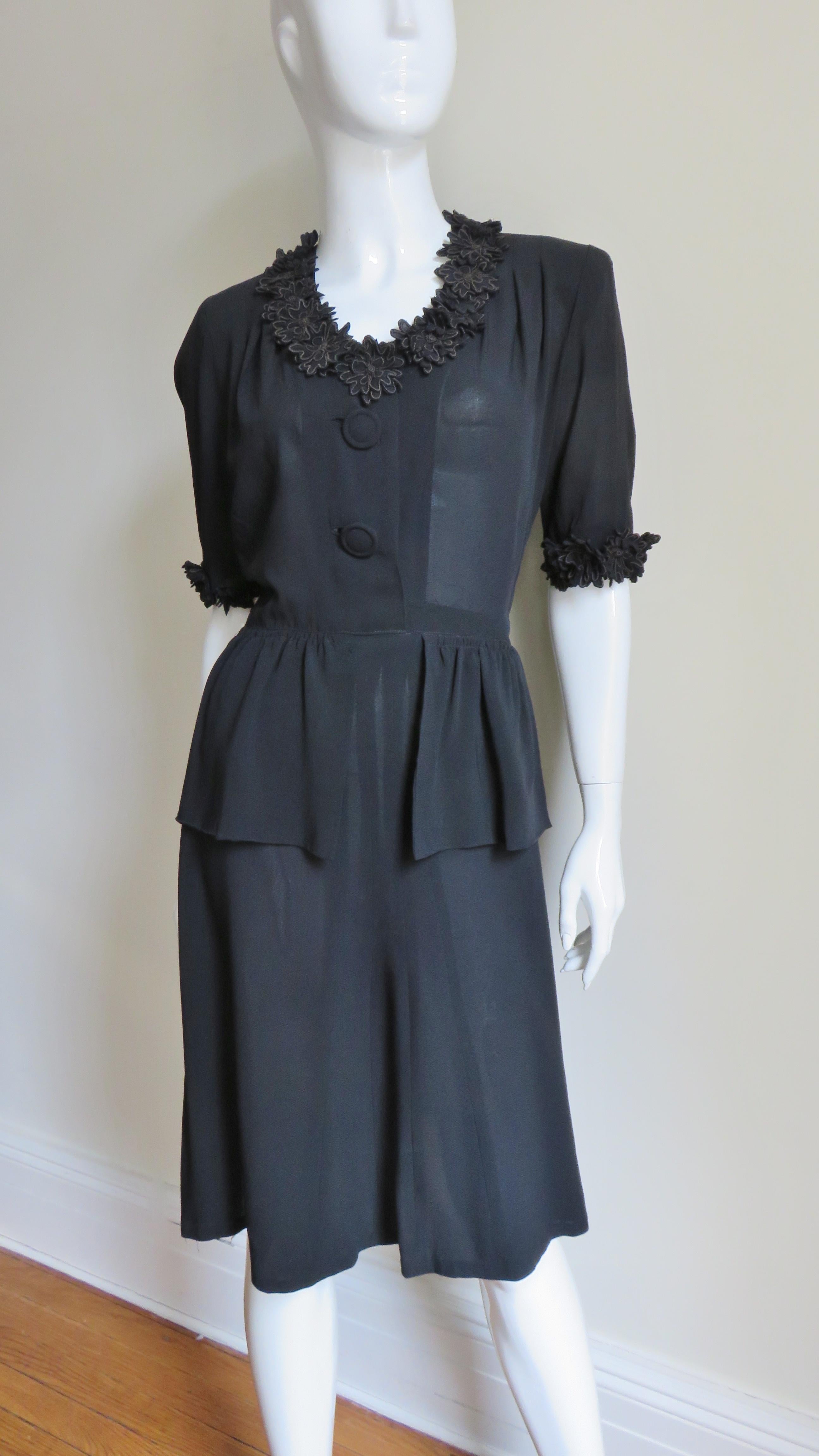A fabulous little black silk 1940s dress. It has a V neckline, elbow length sleeves, shoulder pads and a front peplum on the A line skirt. The bodice front has 2 self covered buttons and bound buttonholes.  The incredible detail includes dozens of