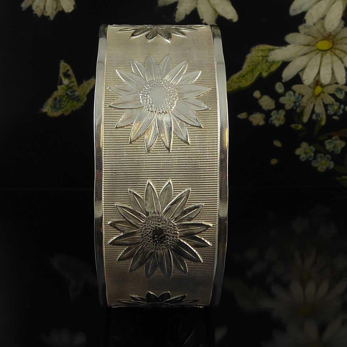 Vintage silver bangle hallmarked at the Chester Assay Office in 1945.  The bangle is adorned with eight daisies against a reeded pattern backround with plain polished edges. Fastening with a buckle style fastener enabling the bangle to be adjusted