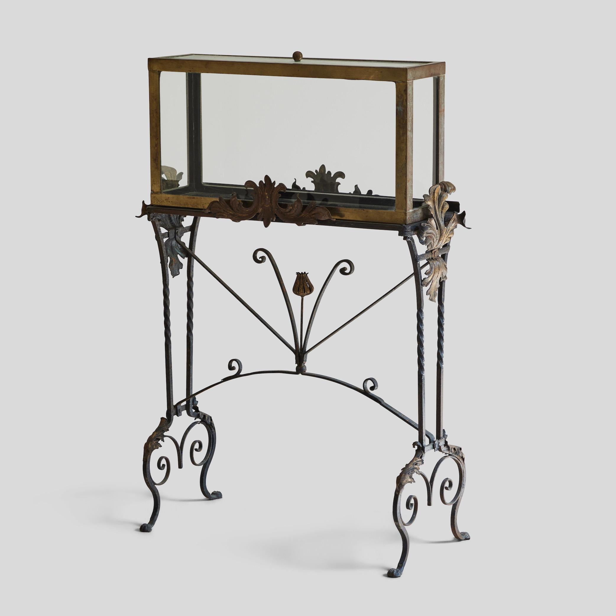 This brass aquarium sits atop a highly adorned iron stand, and a has a textured glass lid. Dating from 1940s Spain, this piece could also serve as a display case. It features a number of floral motifs and worked iron details that make this piece