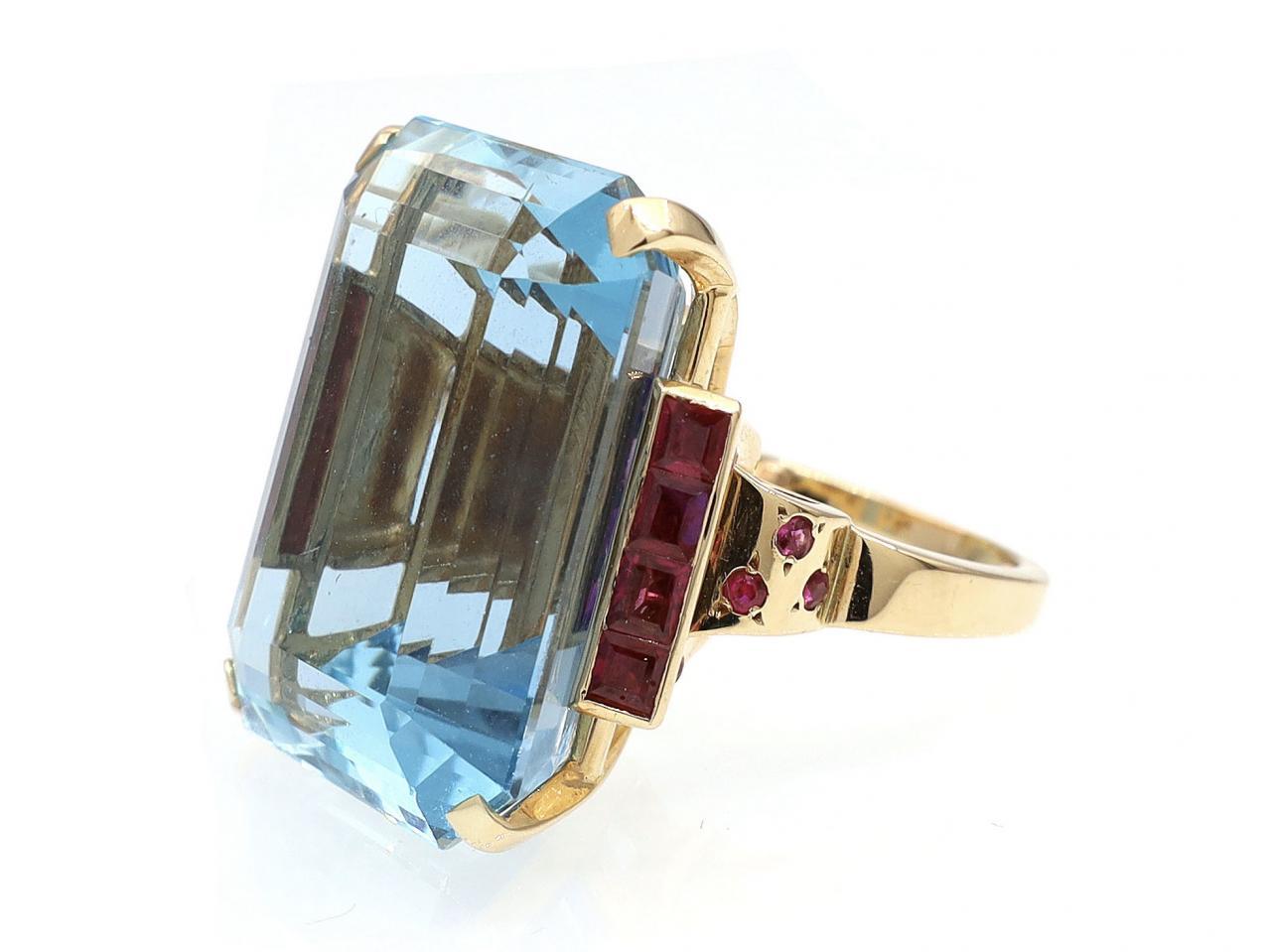1940s Santa Maria 36.86ct aquamarine and Burmese ruby cocktail ring in 18kt yellow gold. Centred with a 36.86ct octagonal step cut Santa Maria aquamarine in a four claw setting, flanked to either side with square step cut Burmese rubies in channel