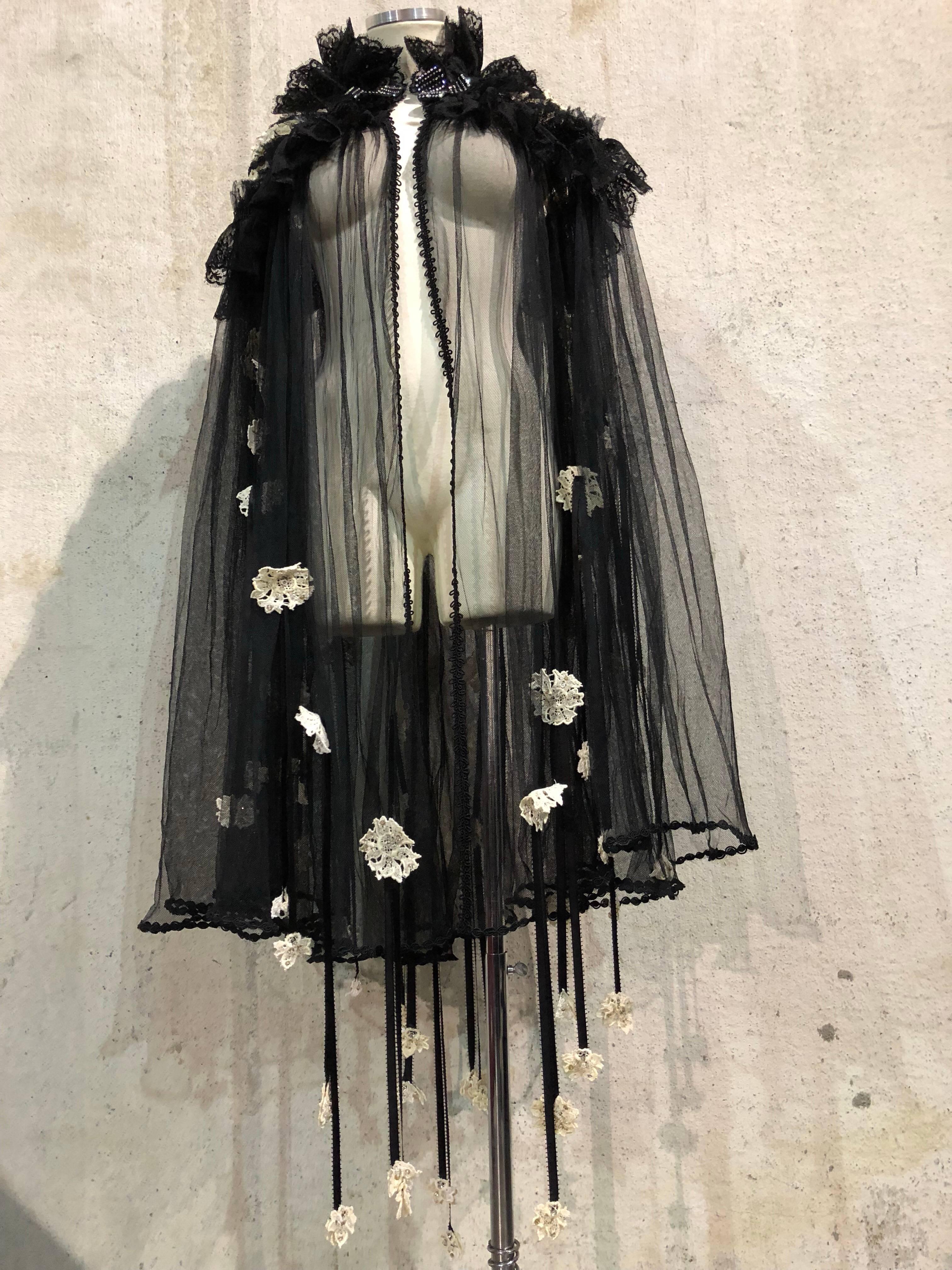 Custom-made 1940s-style black net cape with cotton beaded lace flower applique.  Full collar of black Chantilly lace and net.  Toggle closure at front neckline and cream eyelet details at shoulders. Full swing-cut cape with ribbon streamers