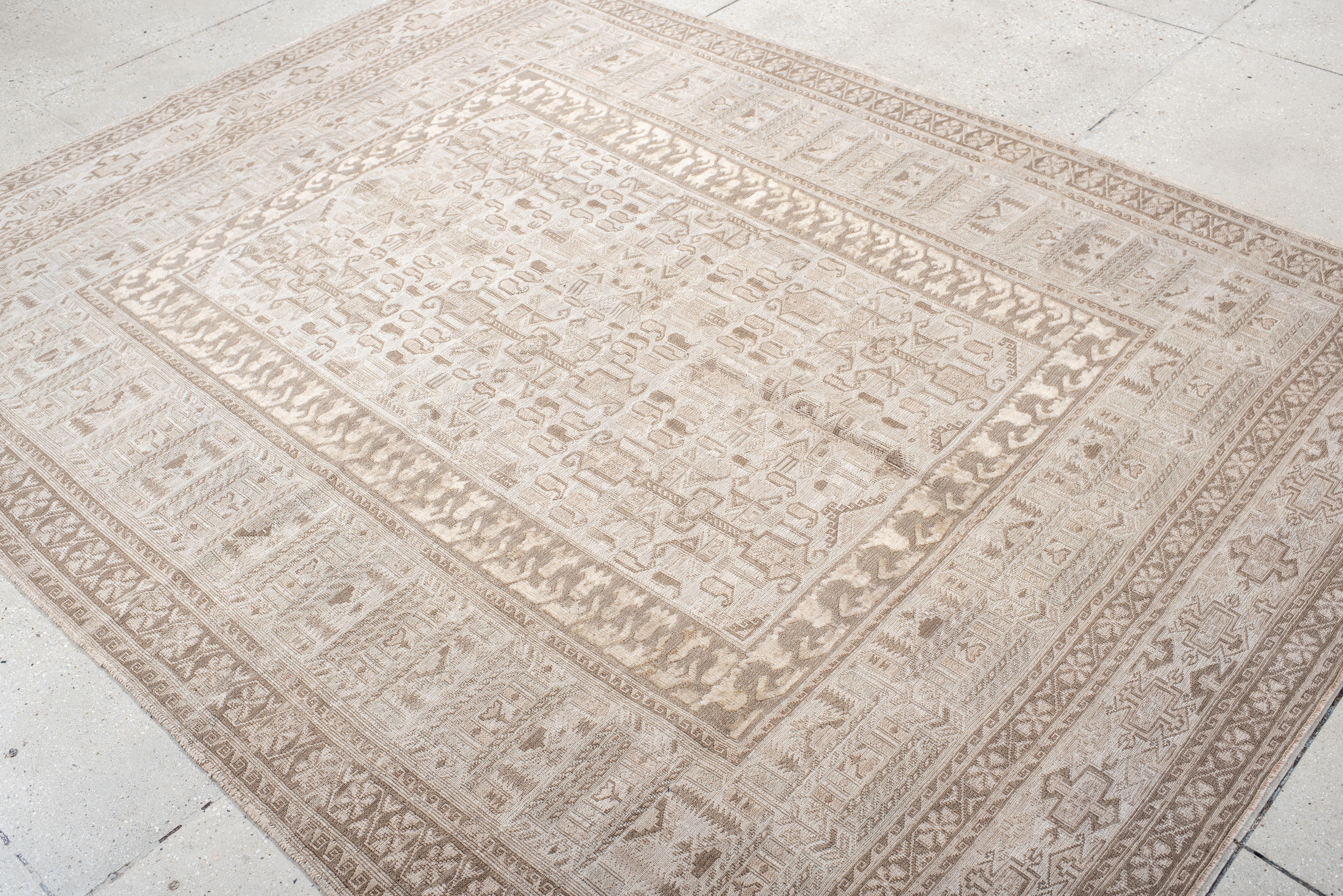 This contemporary Sumak rug is woven in a tightly detailed pattern of tribal symbols and stylized forms, rendered in a sophisticated blend of ivory, flax, and sandstone. The tone-on-tone palette gives the rug a subtle texture and architectural