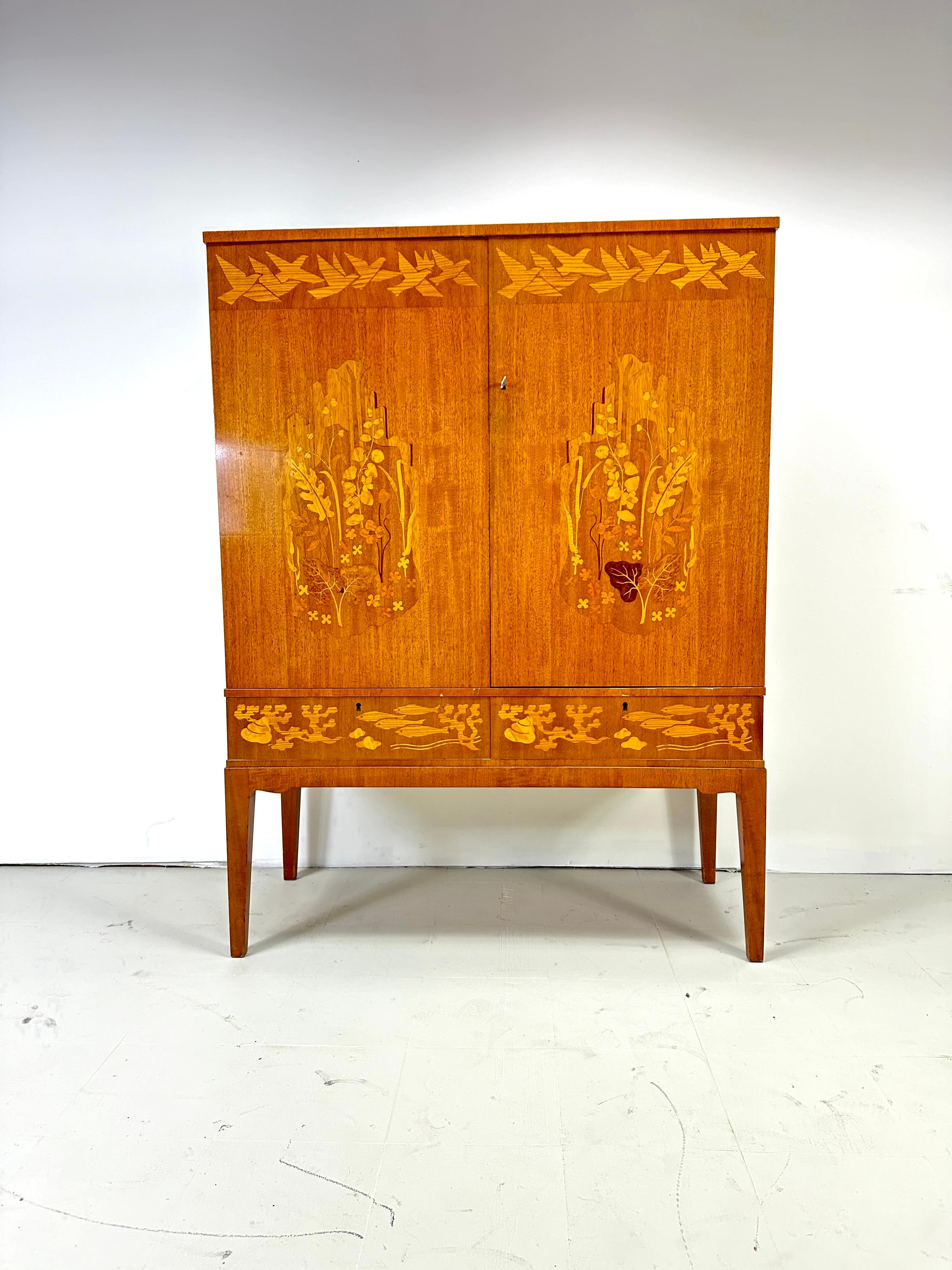 1940’s Swedish Cabinet designed by Erik Mattson. Beautiful intarsia woodworking creating a scene of fish, plants, and birds. Doors conceal interior shelves and drawers. 2 additional front drawers. l
