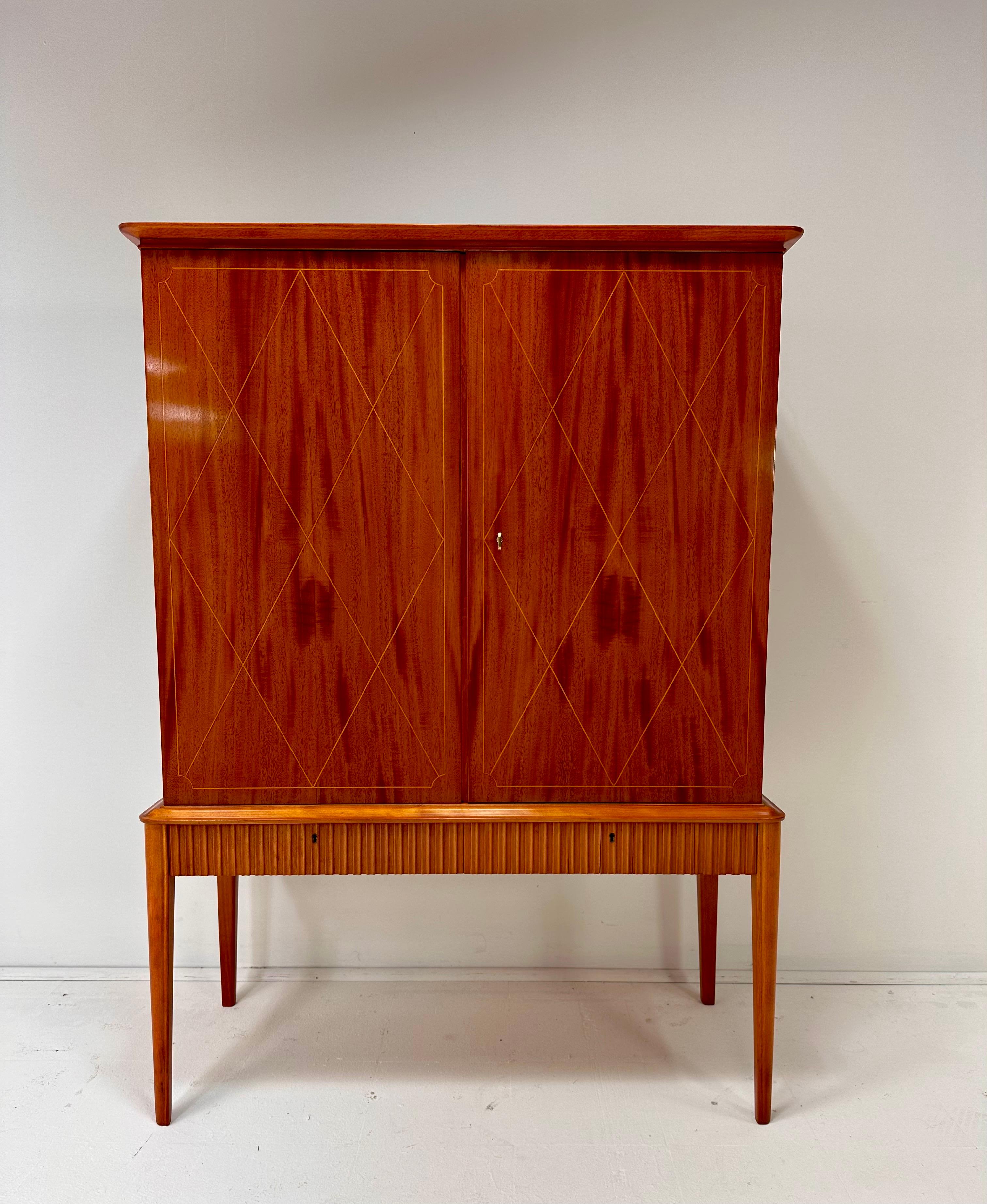 1940’s Swedish Cabinet. Decorative inlay. 2 doors conceal adjustable shelves and 2 drawers. 2 lower drawers with scalloped fronts.  Key included.
