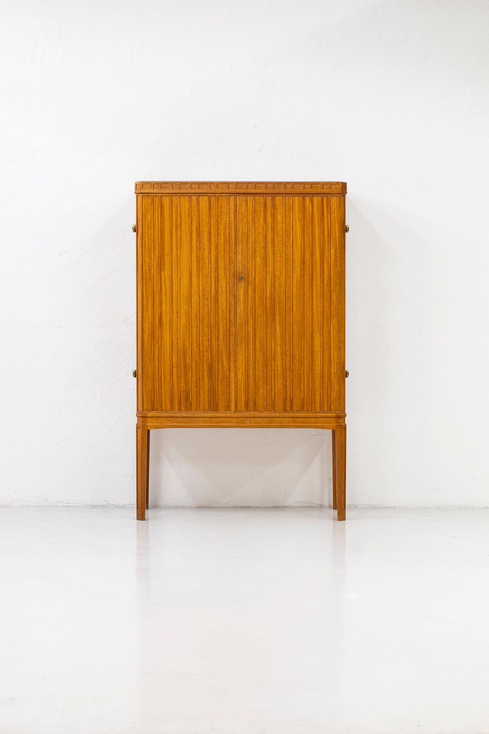 Swedish modern cabinet reminiscent to the style of Oscar Nilsson. Expertly manufactured by a cabinetmaker in Sweden during the 1940s. Made from teak with brass hinges and inside made from maple. With a strict relief pattern on the doors. Good