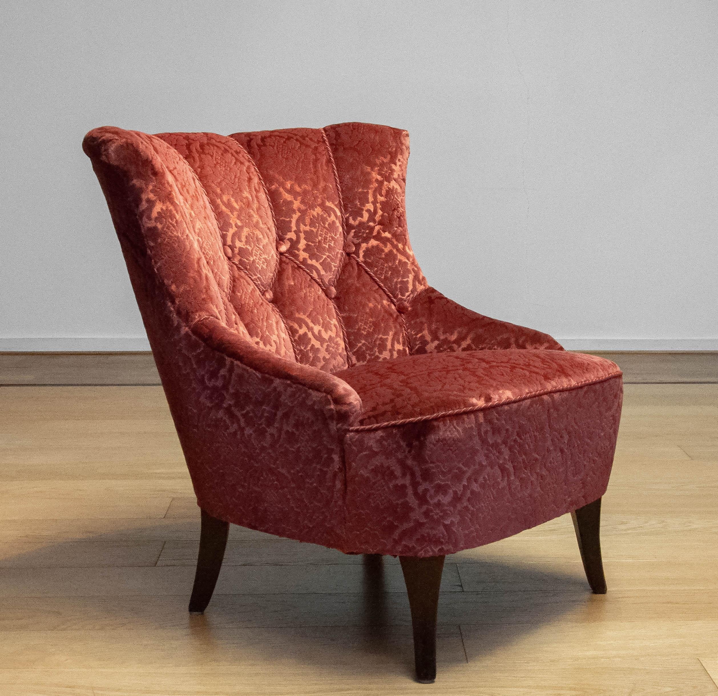Fauteuil suédois des années 1940 de style Napoléon III, tapissé d'un riche tissu jacquard de velours rouge brique. Cette élégante chaise de salon présente un dossier magnifiquement sculpté avec de profonds capitons et des accoudoirs doux et arrondis