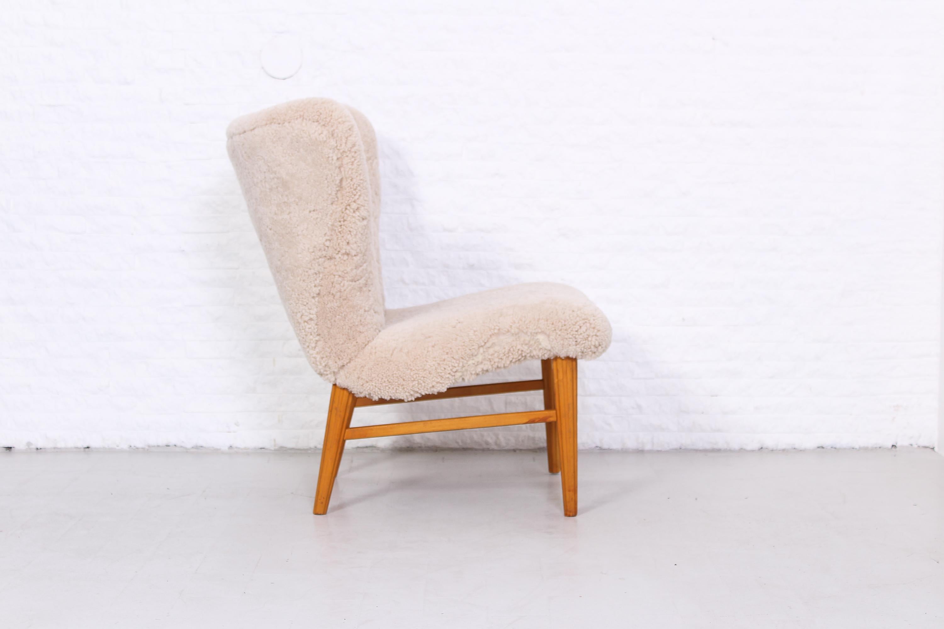 A Swedish easy chair, most likely designed by Eric Carlén. Manufactured in the 1940s with new sheepskin upholstery. This beautiful chair has many interesting features such as the large curved backrest. Very good vintage condition with new upholstery.