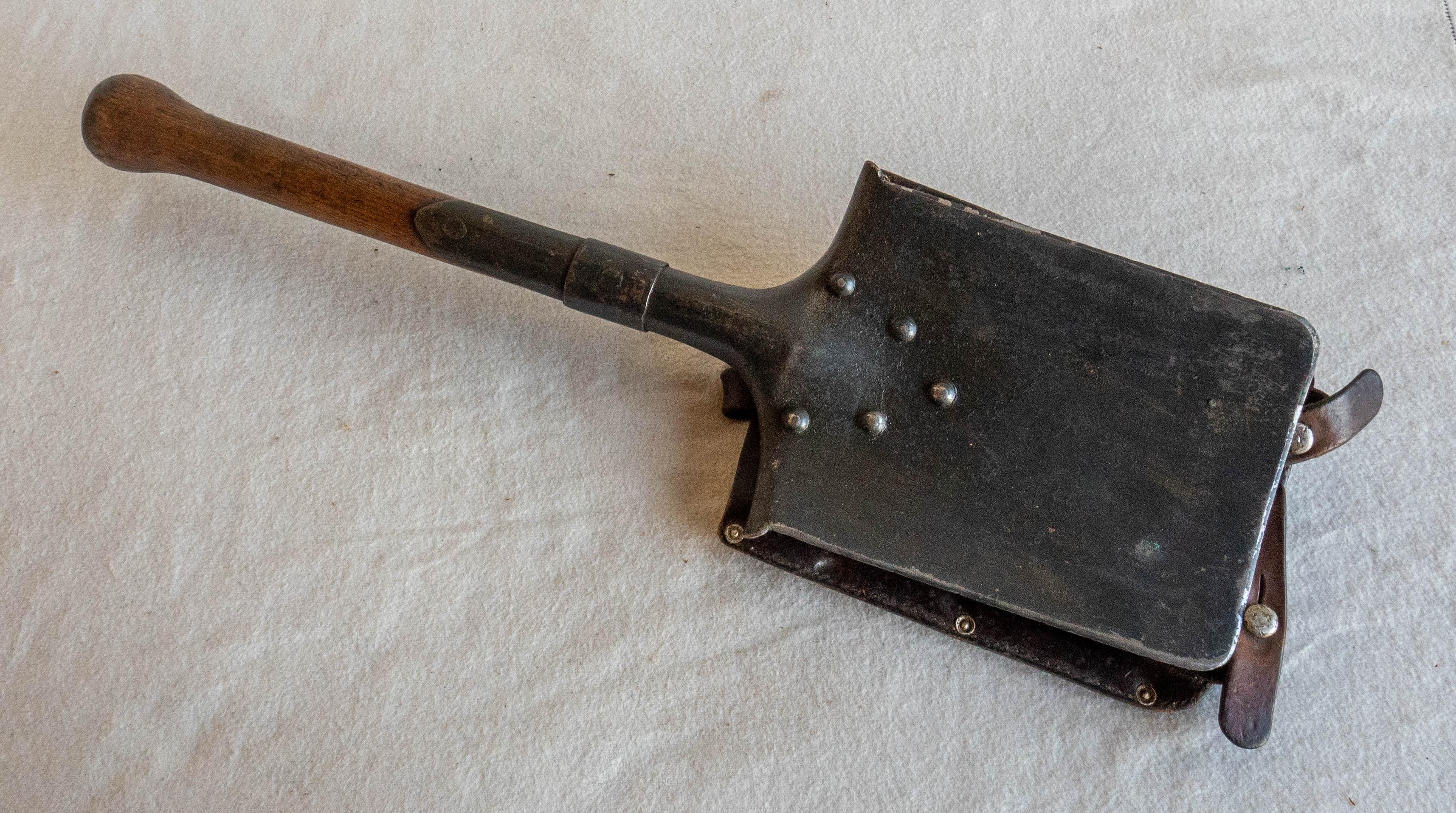 A military grade forged metal shovel with a protective leather cover used by the Swiss Army mountaineers during World War II.