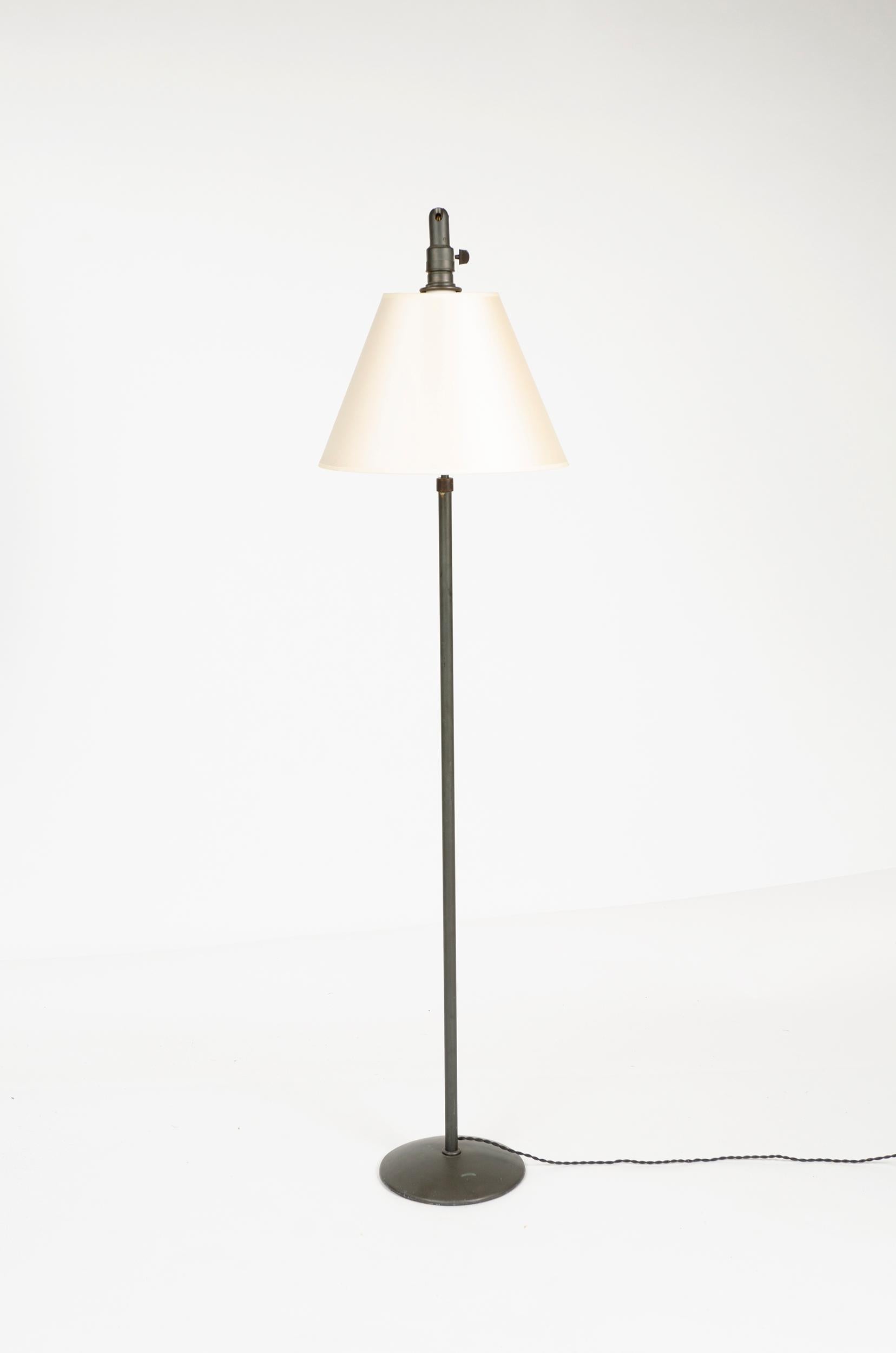 A vertically telescoping brass floor lamp with shade on a pivoting neck.