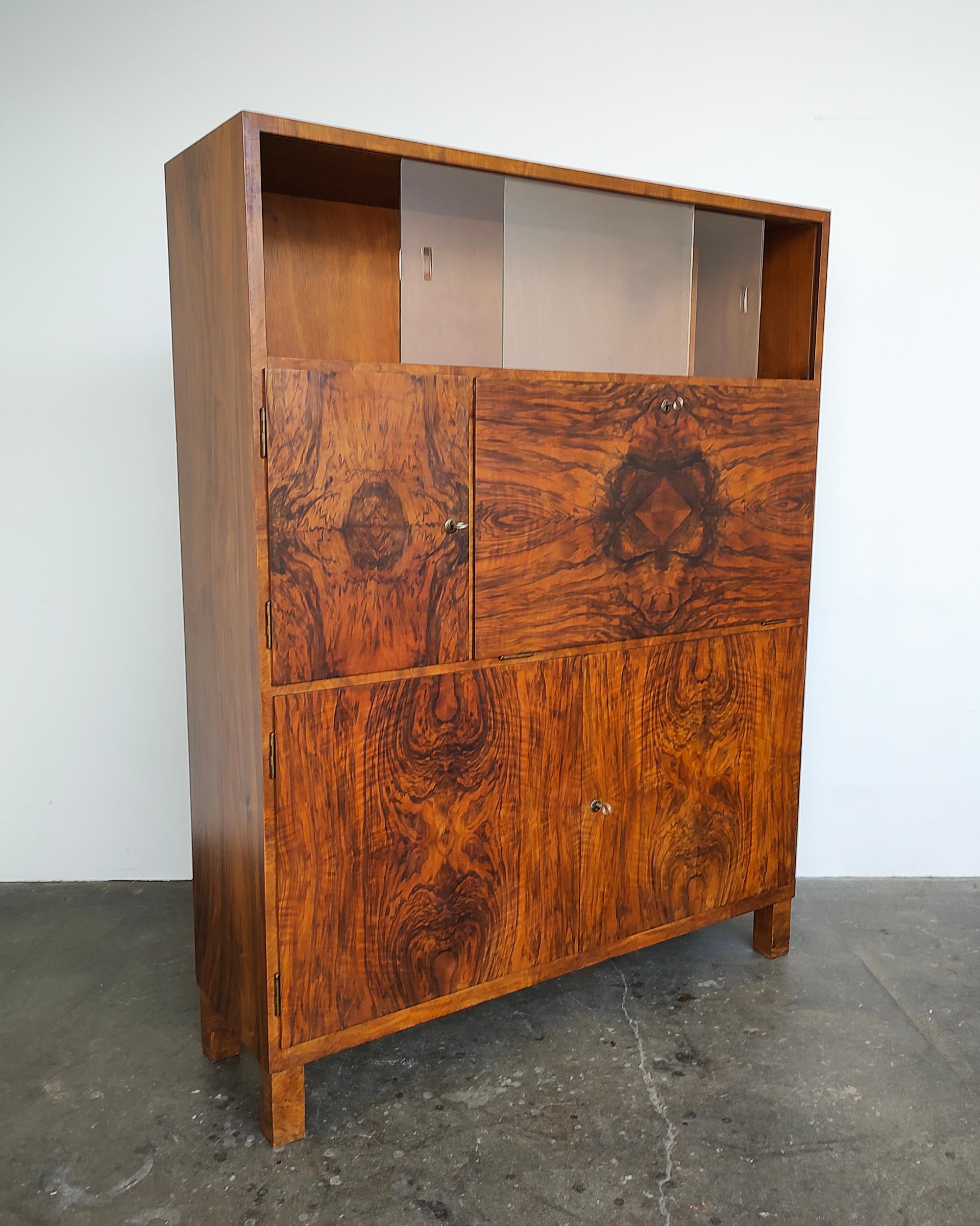 Walnut burl wood Swiss bar cabinet circa 1930-1940. Gorgeous wood grain covering all cabinet faces. Upper area features sliding glass doors with recessed pulls. Fold-down locking cabinet middle right with two small drawers inside. Middle locking