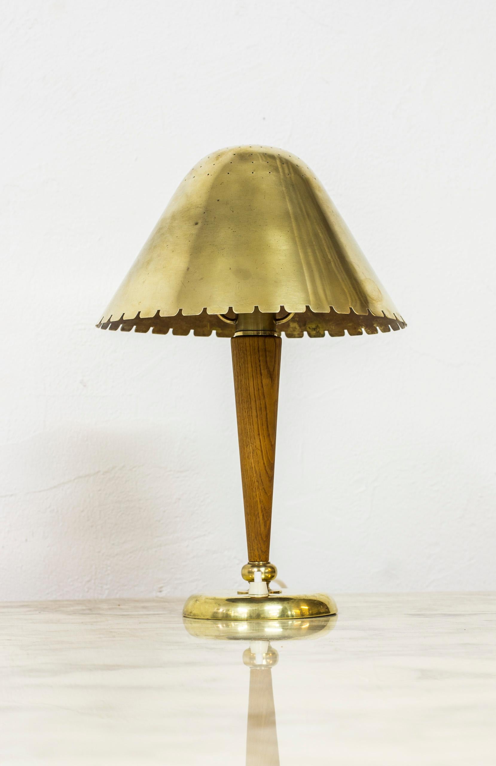 Small table lamp attributed to Harald Elof Notini in Sweden during the 1940s. Likely produced by Böhlmarks in Stockholm, Sweden. Solid oak and brass base with perforated brass shade. Light switch on the base in working condition. Good condition with