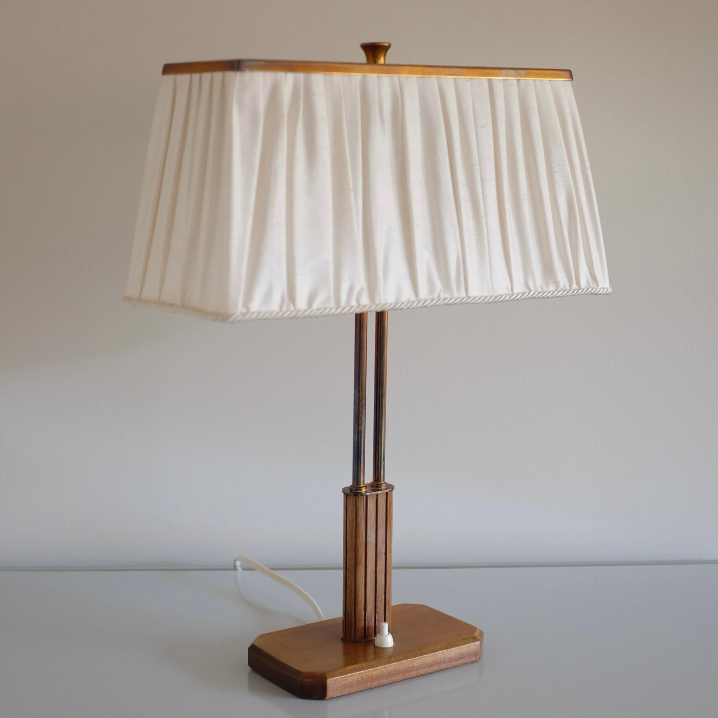 Magnifique lampe de table des années 1940, modèle 15485 de Böhlmarks, Suède, peut-être conçue par Harald Notini. Pied de lampe en bois avec détails sculptés et laiton. Il y a 2 lumières sous un abat-jour en soie surmonté d'une plaque en laiton et de