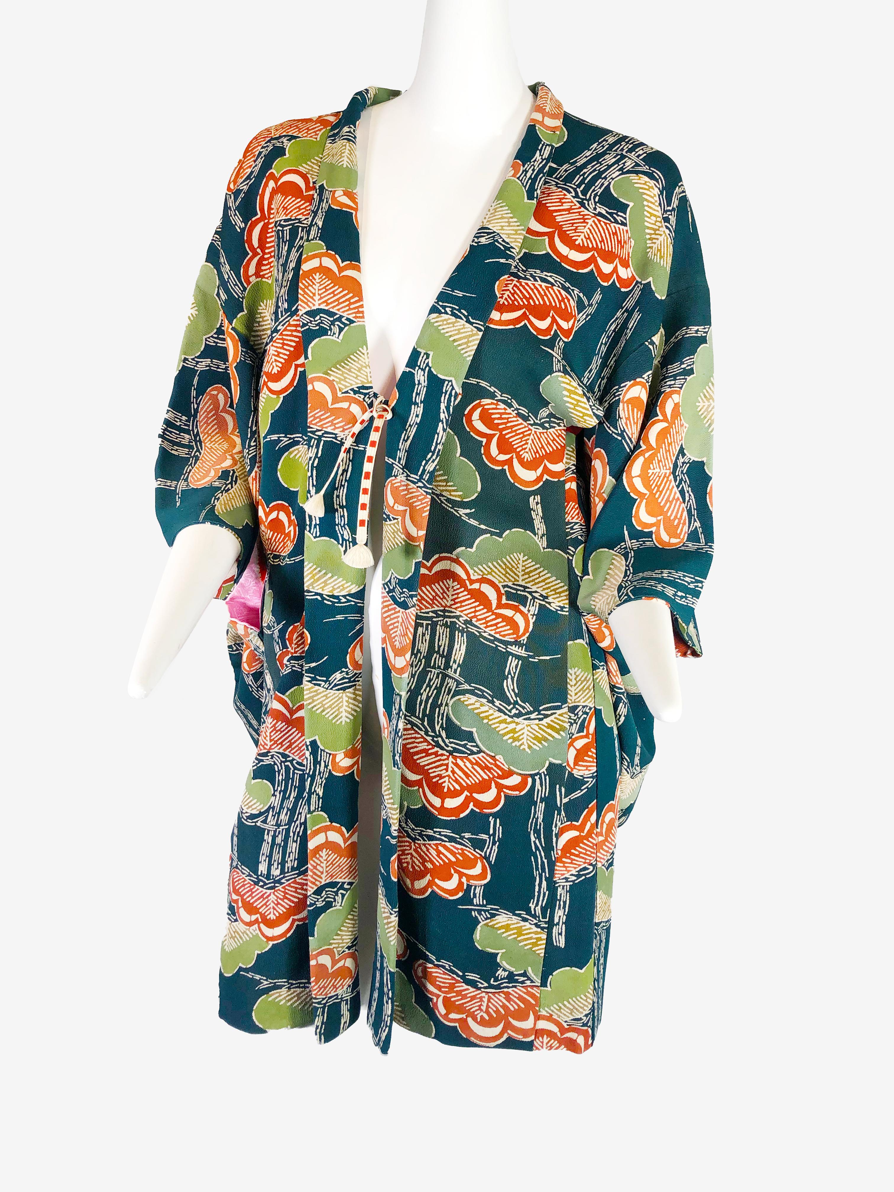 A 1940s traditionally-styled silk kimono: knee-length with a stylized ginkgo leaf print in an olive green persimmon and black colorway. Traditional contrasting silk lining in top half is fashioned of a beautiful pink and orange tie-dyed pattern.
