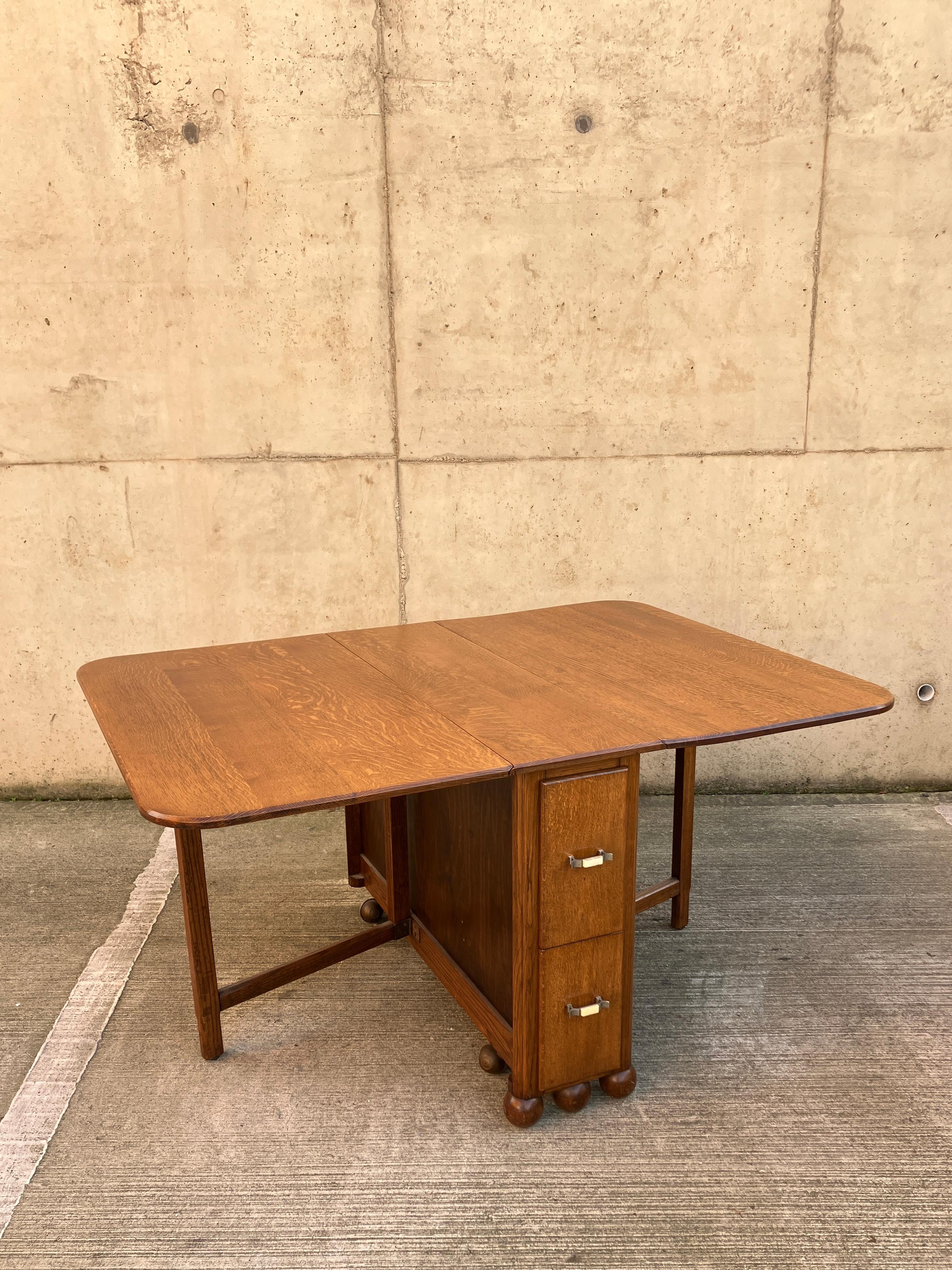 English antique folding dining table from 1940's in Oak. Unique design with two sets of extra deep long drawers and beautiful ball feet. Bakelite handles. A great versatile table suitable for the dining room or an office. 
Fantastic condition for
