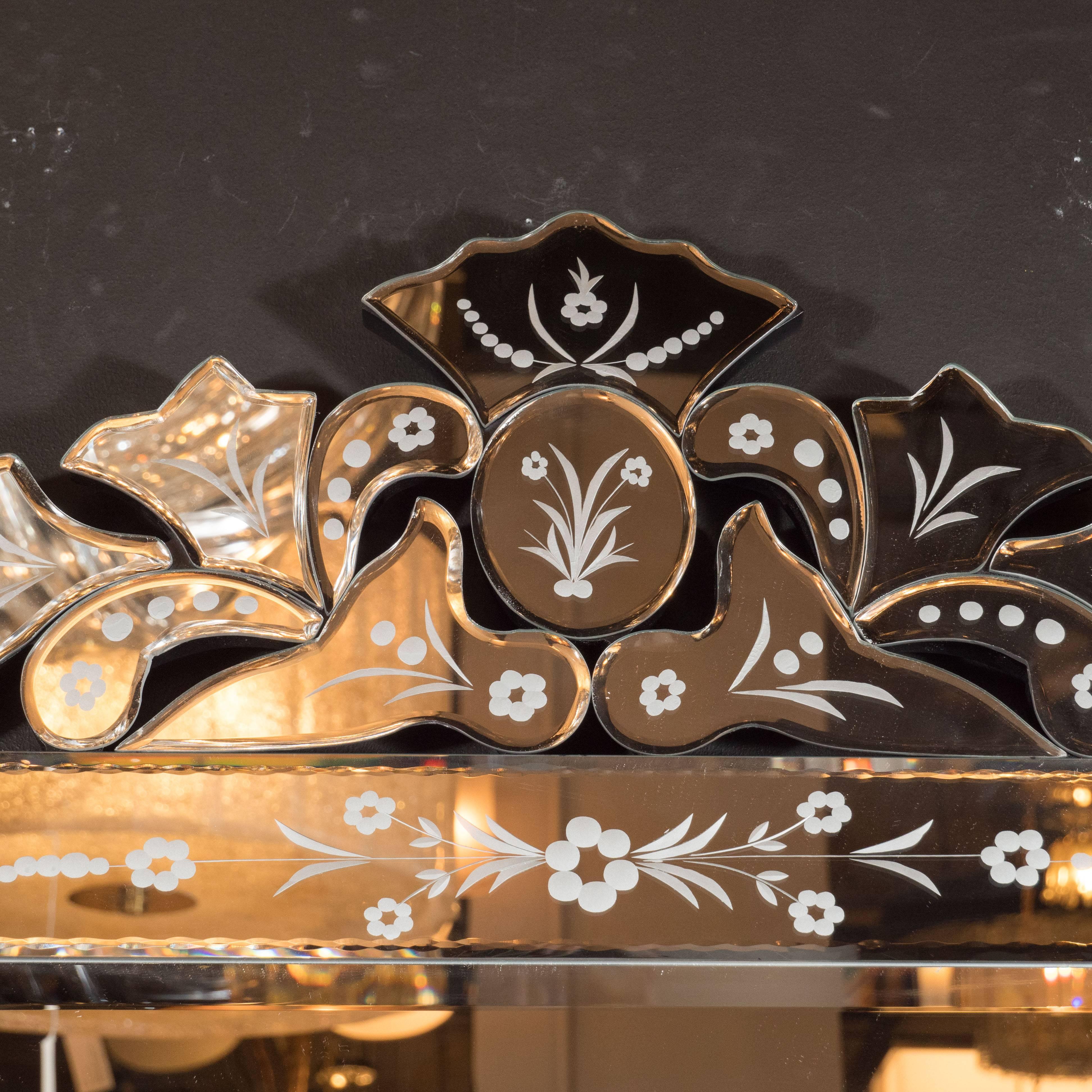This glamorous 1940s Hollywood style Venetian mirror features stylized floral motifs throughout; reverse etched abstracted foliate forms adorning the top; and bevel and chain detailing circumscribing the interior and exterior perimeters of the