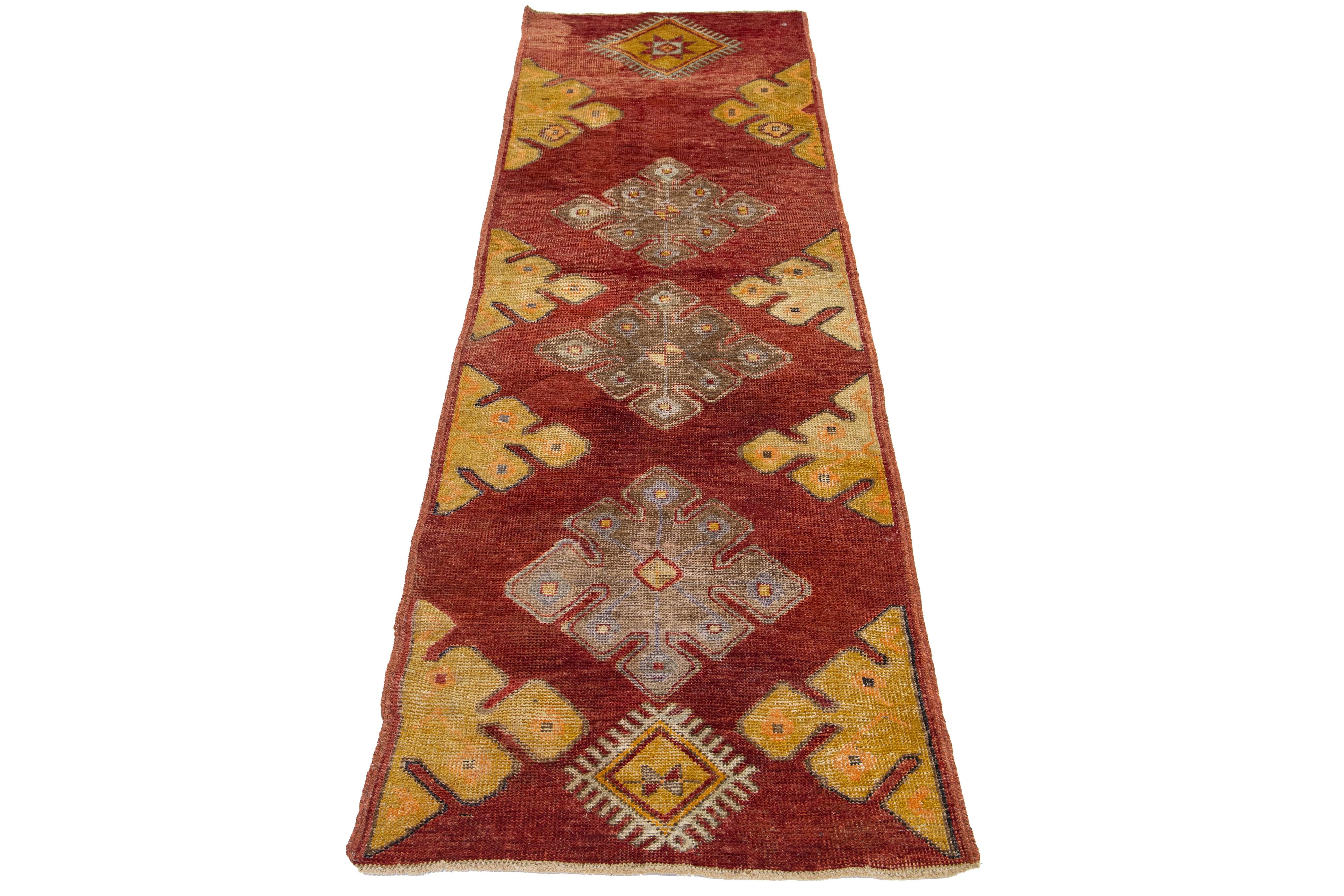 Ein schöner türkischer Läufer im Vintage-Stil mit einem roten Feld und einem geometrischen Stammesmuster, das sich über den gesamten Teppich erstreckt, mit hellbraunen und gelben Akzenten.

Dieser Teppich misst 2'4