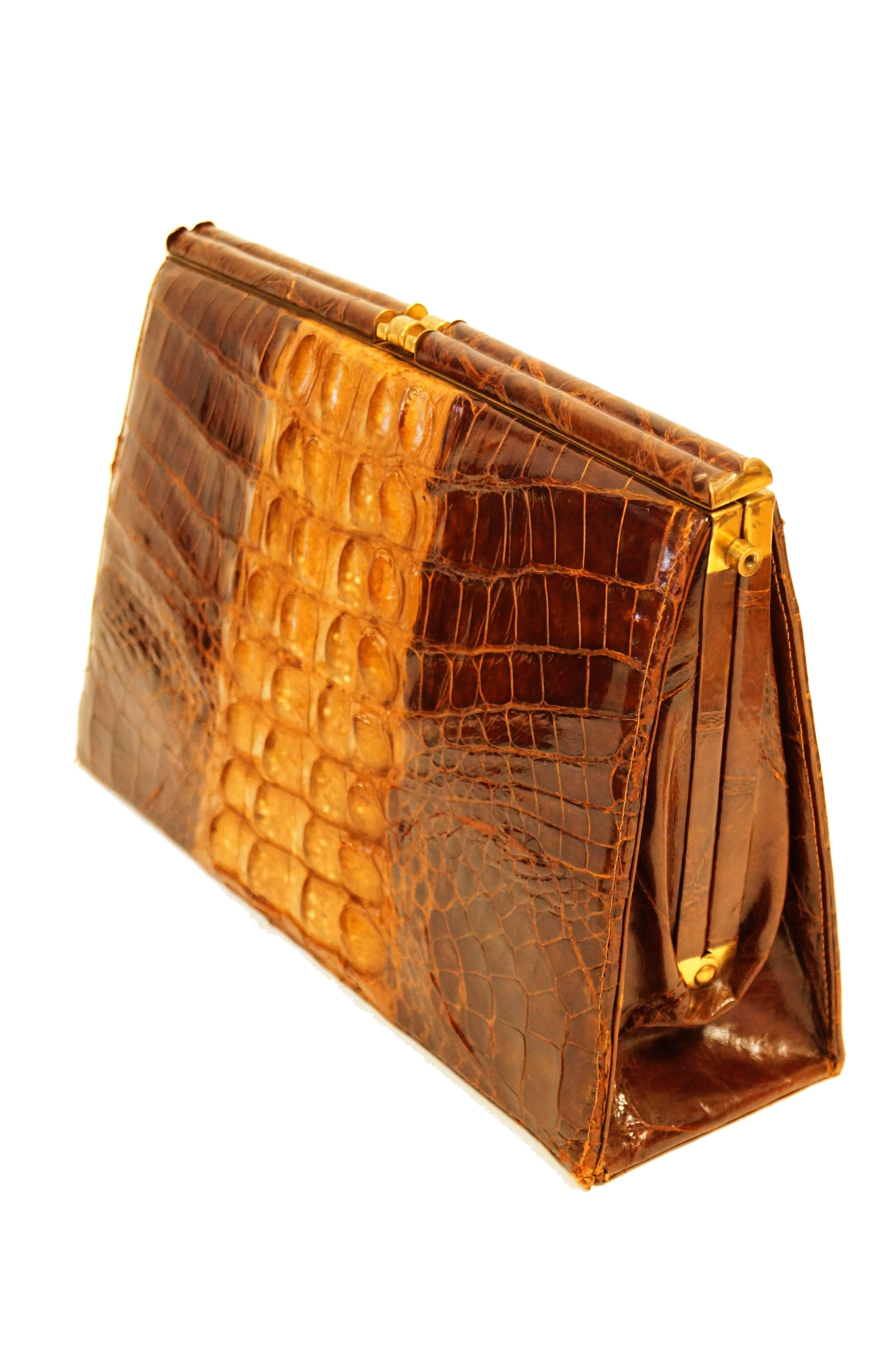Statement  mid-century A - frame clutch in honey / walnut - tone alligator skin. The clutch has a center compartment featuring multiple open and zippered pockets. Brown flocked lining.