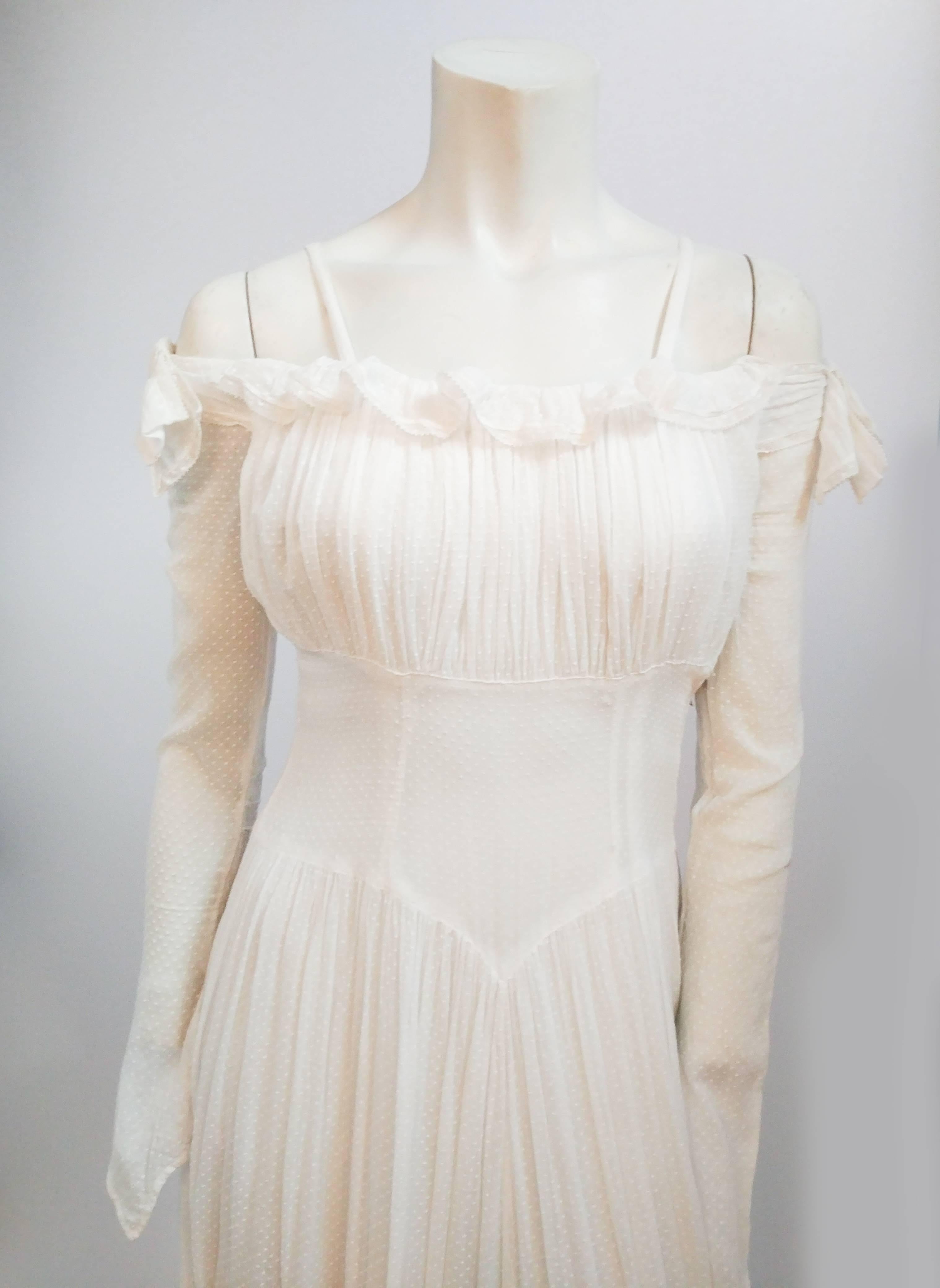 robe de mariée blanche à pois suisse des années 1940. Les épaules sont ornées de petits volants. Les manches longues arrivent à un point à la main. Buste froncé et basque à la taille. Une traîne pleine longueur dans le dos. 