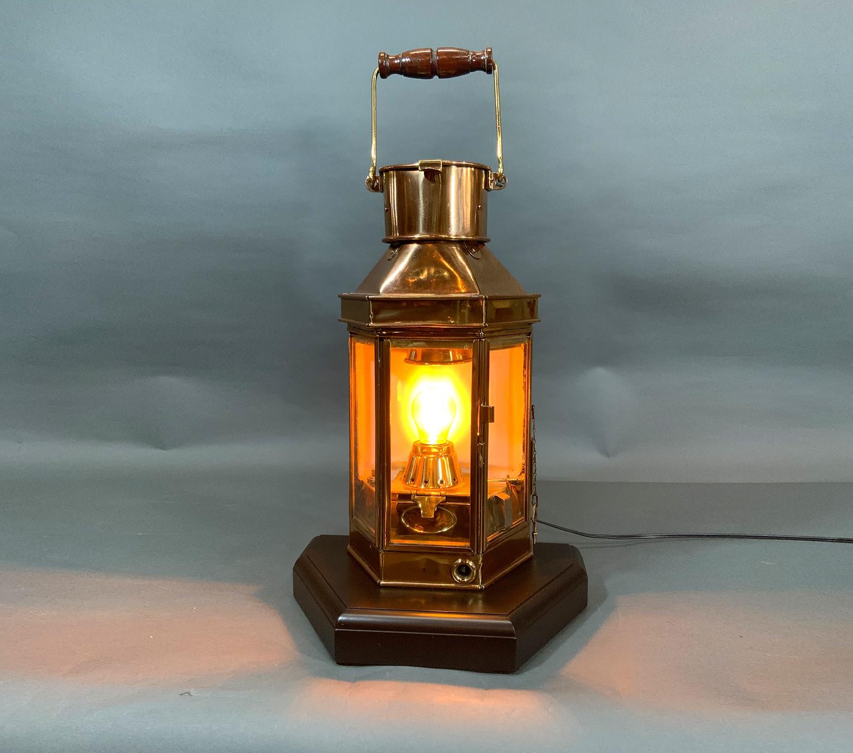 Ships lantern with engraved chimney with makers name Alderson and Co LTD, Birmingham 1941. Case has three glass panels with one hinged. Mounted to a thick mahogany base, carry handle with wood handle. Electric socket fitted to oil socket for home